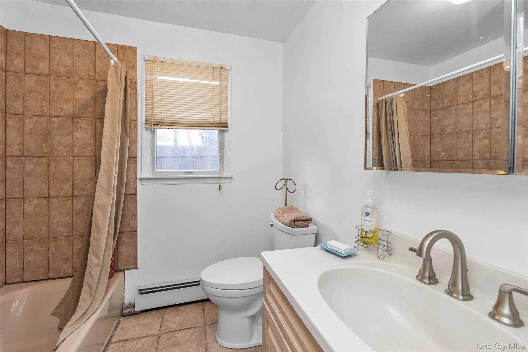 Bathroom with vanity, shower / bath combination with curtain, a baseboard heating unit, and light tile patterned floors Bathroom with vanity, shower / bath combination with curtain, a baseboard heating unit, and light tile patterned floors