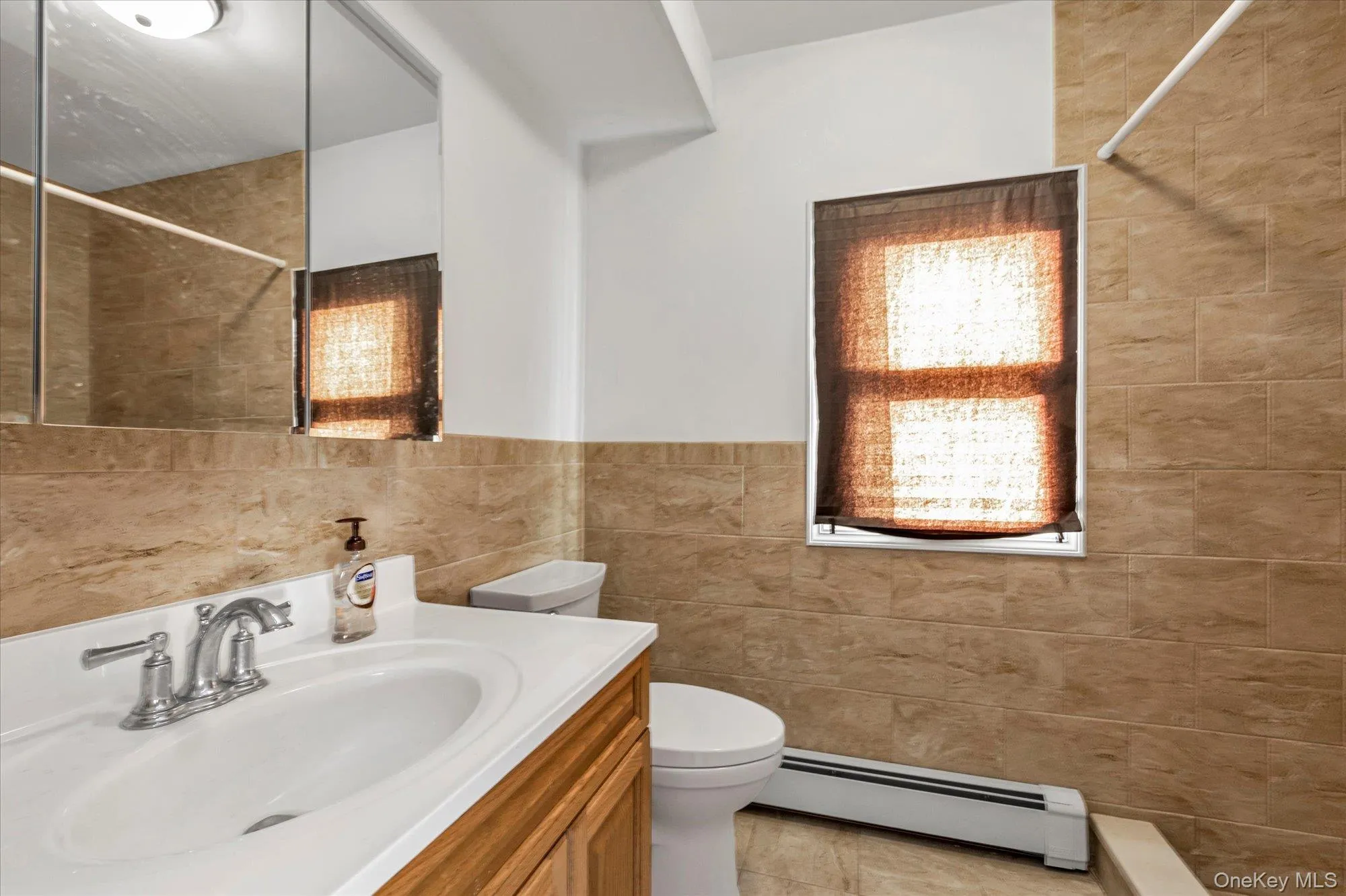 Full bath with vanity, a baseboard heating unit, tiled shower, tile walls, and light tile patterned flooring Full bath with vanity, a baseboard heating unit, tiled shower, tile walls, and light tile patterned flooring