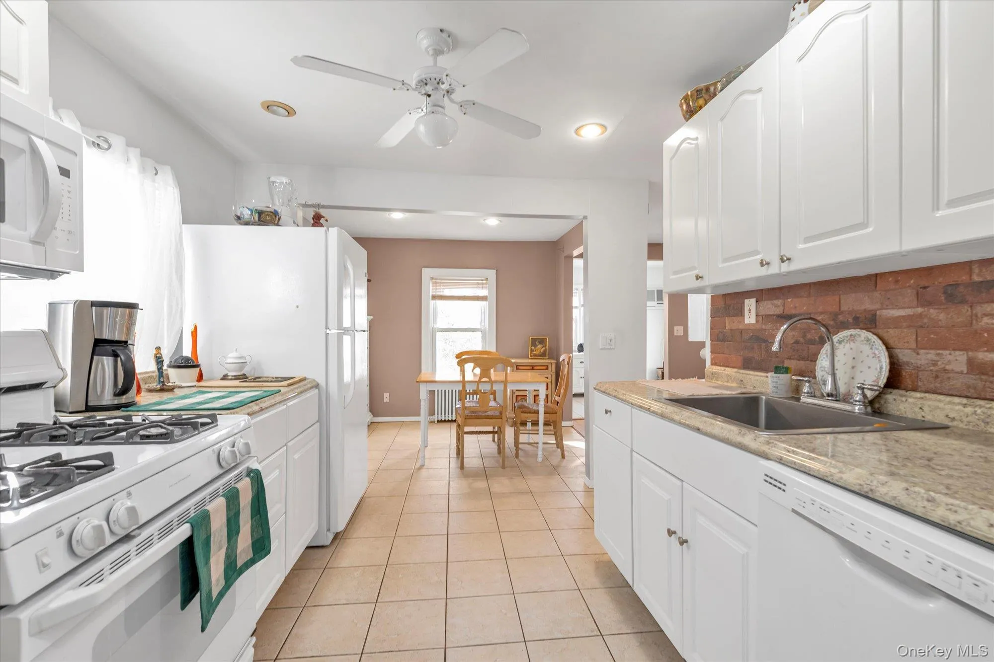 Kitchen featuring white appliances, white cabinetry, light countertops, decorative backsplash, and light tile patterned flooring Kitchen featuring white appliances, white cabinetry, light countertops, decorative backsplash, and light tile patterned flooring