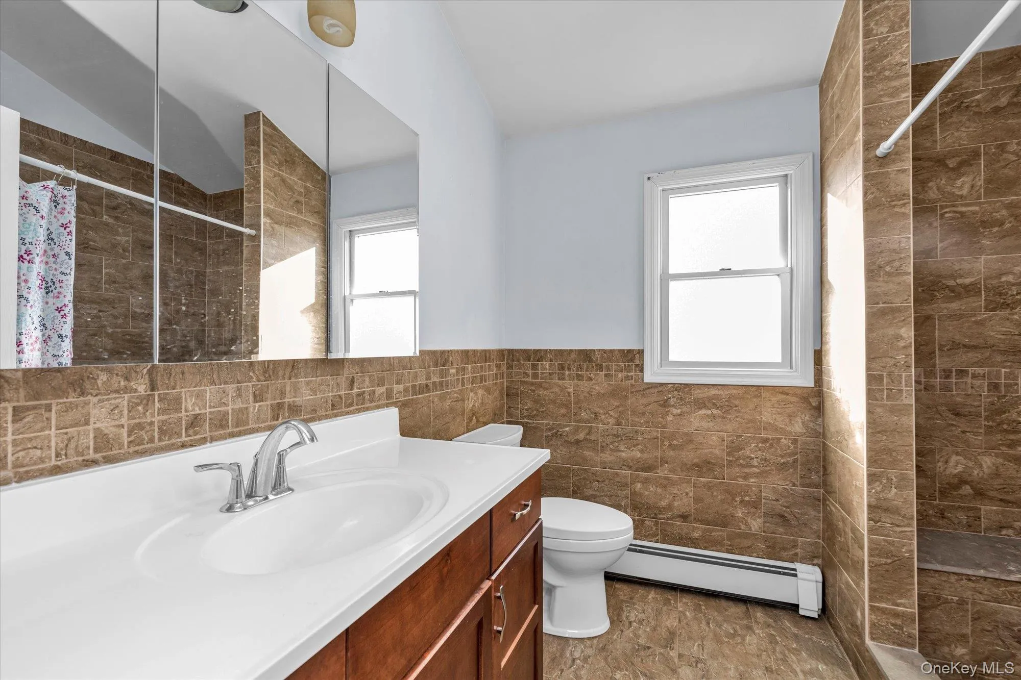 Bathroom featuring tiled shower, tile walls, a baseboard radiator, vanity, and a wainscoted wall Bathroom featuring tiled shower, tile walls, a baseboard radiator, vanity, and a wainscoted wall