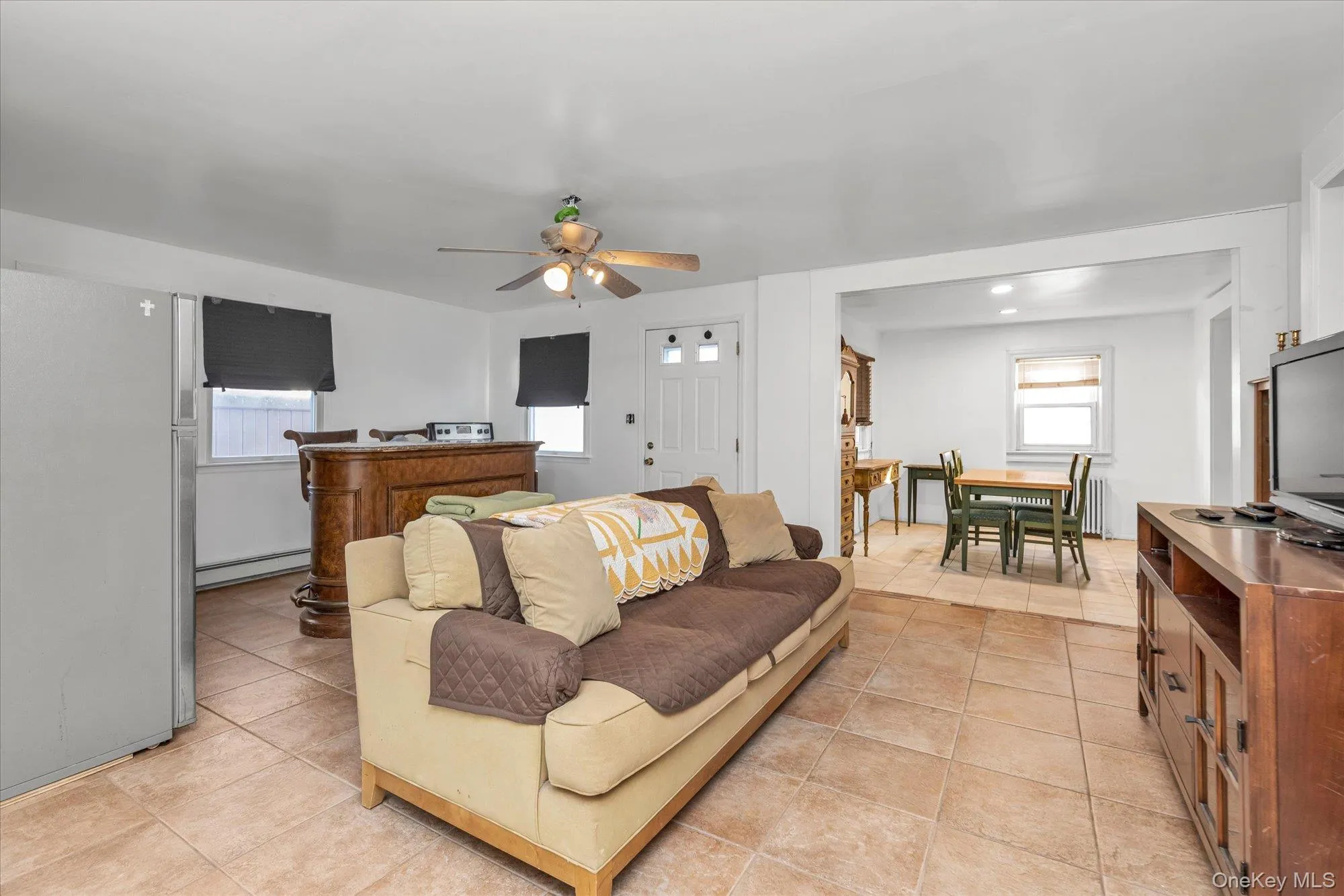 Living room with light tile patterned floors, a ceiling fan, and a baseboard radiator Living room with light tile patterned floors, a ceiling fan, and a baseboard radiator