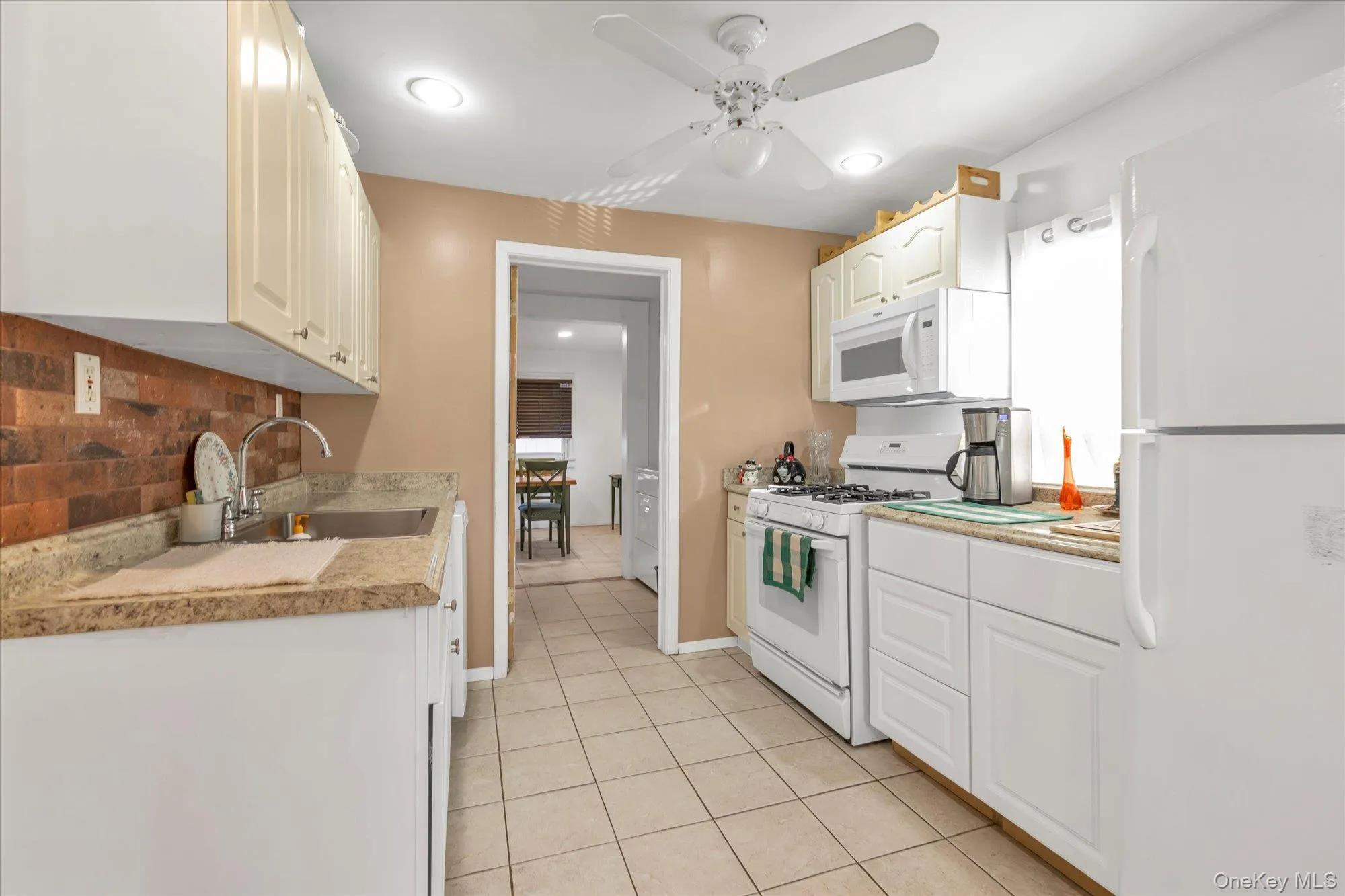 Kitchen featuring white appliances, light countertops, light tile patterned floors, ceiling fan, and white cabinetry Kitchen featuring white appliances, light countertops, light tile patterned floors, ceiling fan, and white cabinetry