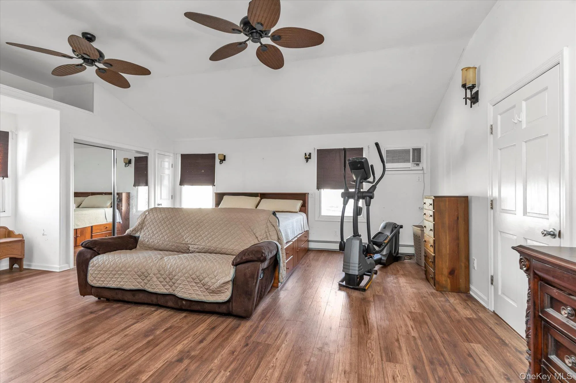 Bedroom featuring vaulted ceiling, a closet, a ceiling fan, wood finished floors, and a wall unit AC Bedroom featuring vaulted ceiling, a closet, a ceiling fan, wood finished floors, and a wall unit AC