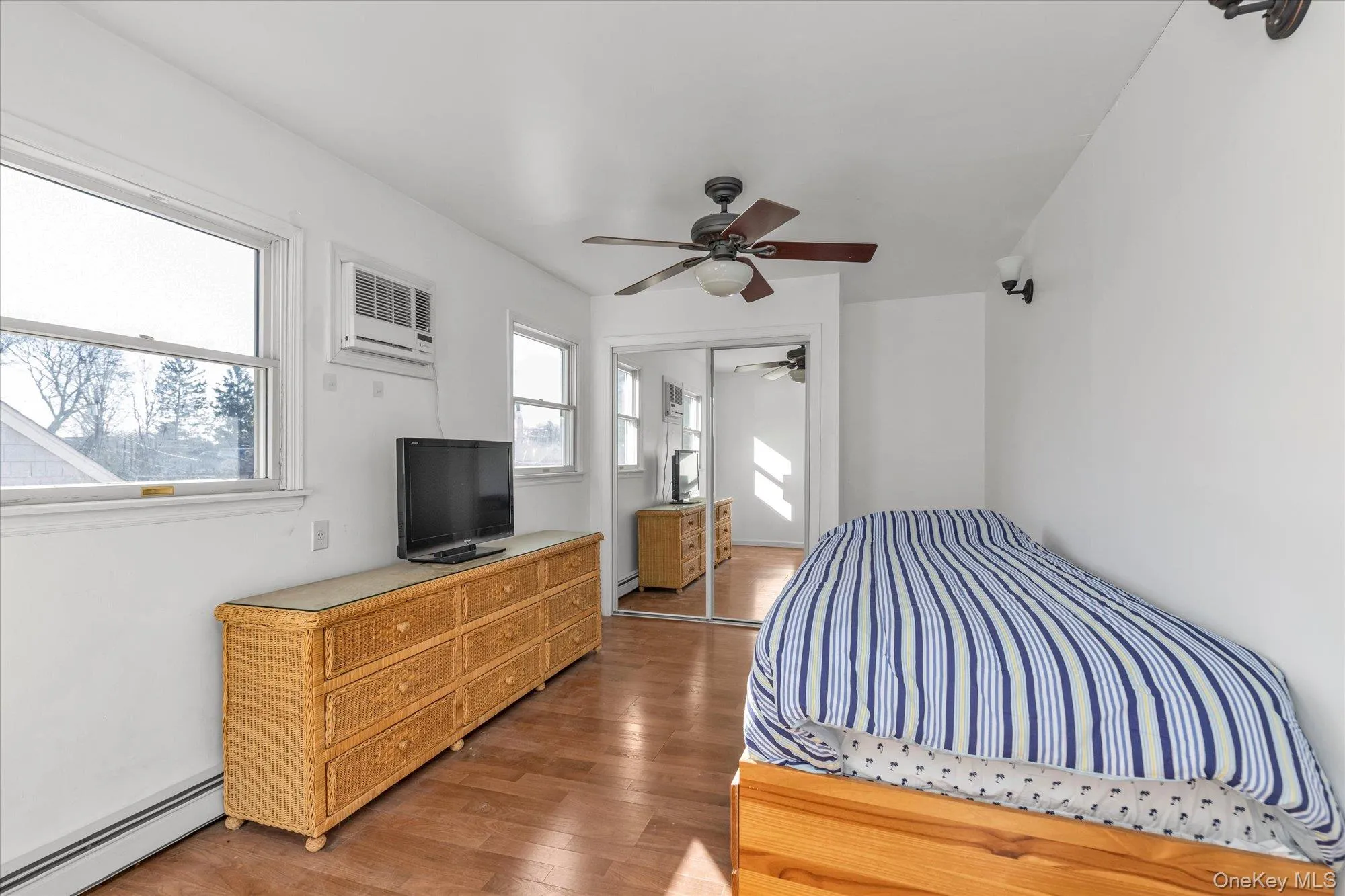 Bedroom with a baseboard radiator, ceiling fan, light wood-style floors, a closet, and a wall unit AC Bedroom with a baseboard radiator, ceiling fan, light wood-style floors, a closet, and a wall unit AC