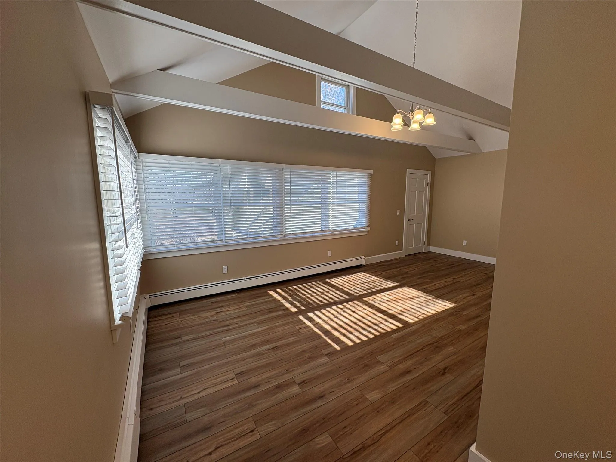 Unfurnished room with dark wood-style floors, a chandelier, and baseboard heating Unfurnished room with dark wood-style floors, a chandelier, and baseboard heating