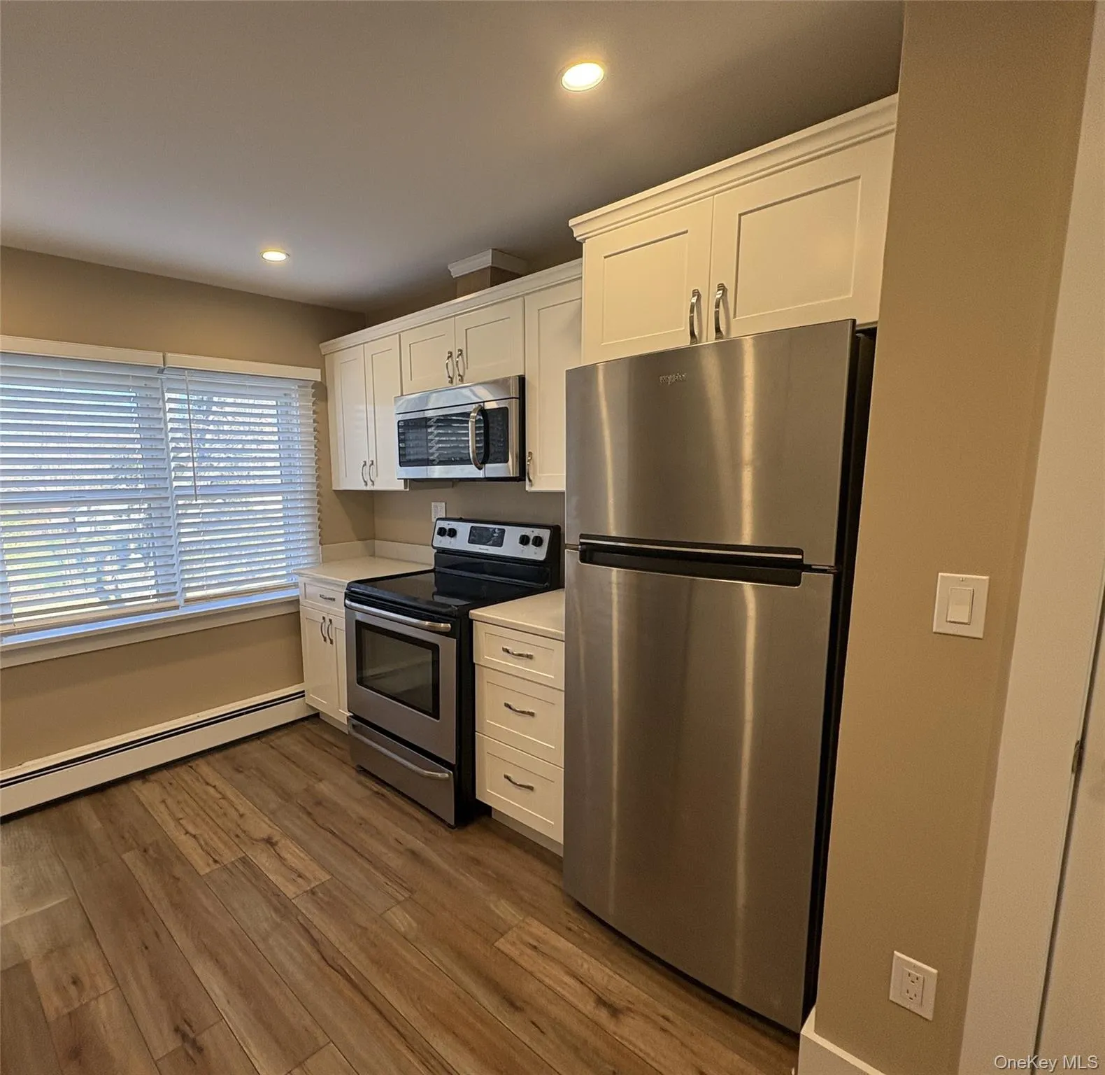 Kitchen featuring stainless steel appliances, white cabinets, light countertops, recessed lighting, and dark wood finished floors Kitchen featuring stainless steel appliances, white cabinets, light countertops, recessed lighting, and dark wood finished floors