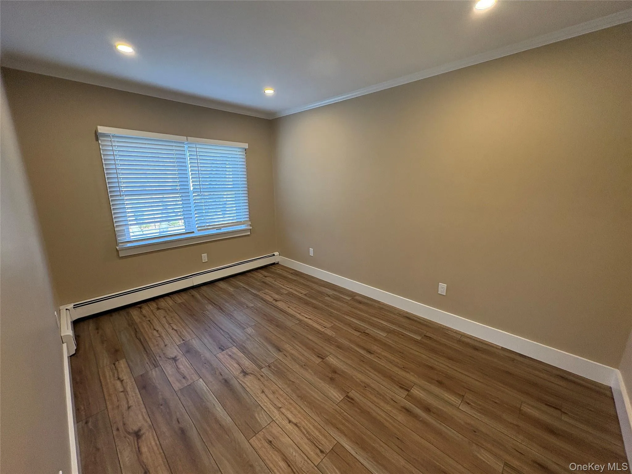 Empty room with dark wood-style floors, recessed lighting, ornamental molding, and a baseboard heating unit Empty room with dark wood-style floors, recessed lighting, ornamental molding, and a baseboard heating unit