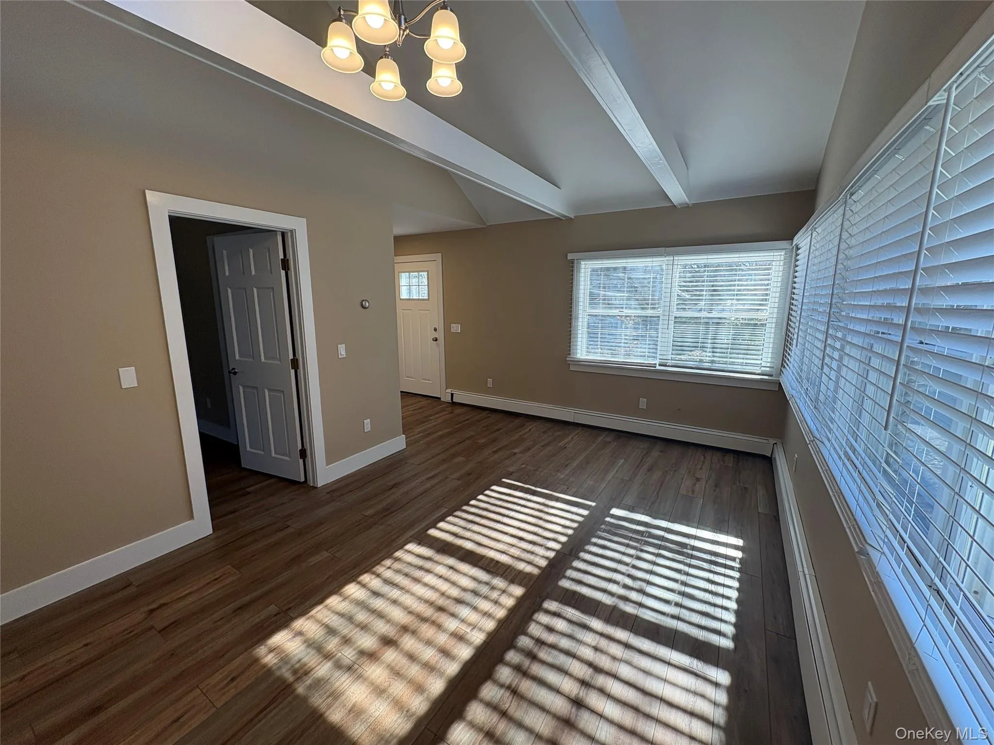 Unfurnished room with dark wood-style floors, a chandelier, plenty of natural light, and a baseboard radiator Unfurnished room with dark wood-style floors, a chandelier, plenty of natural light, and a baseboard radiator