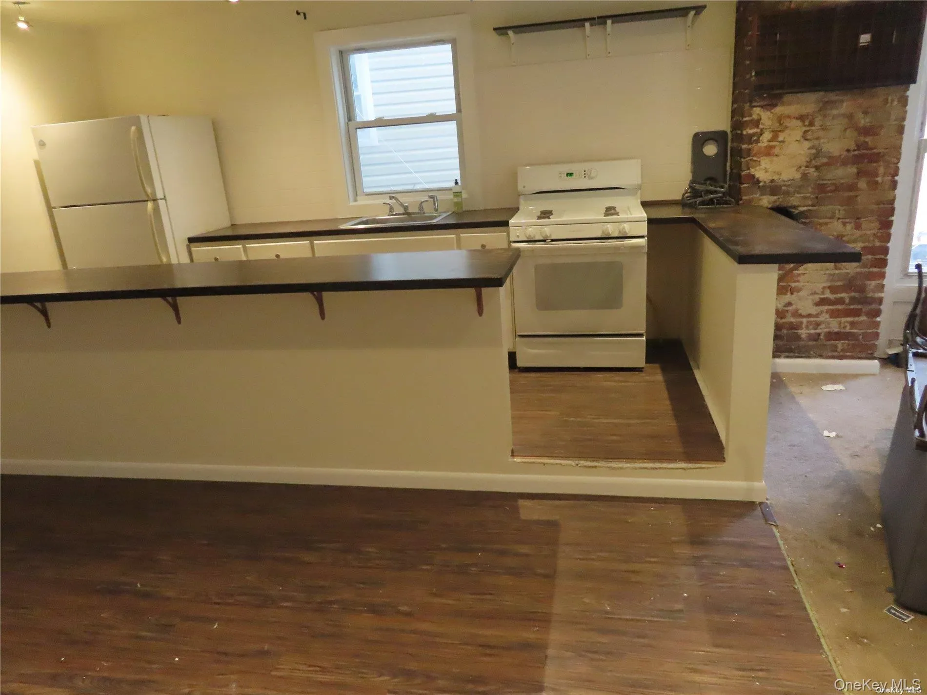 Kitchen featuring white appliances, dark countertops, a breakfast bar area, and dark wood-style flooring Kitchen featuring white appliances, dark countertops, a breakfast bar area, and dark wood-style flooring