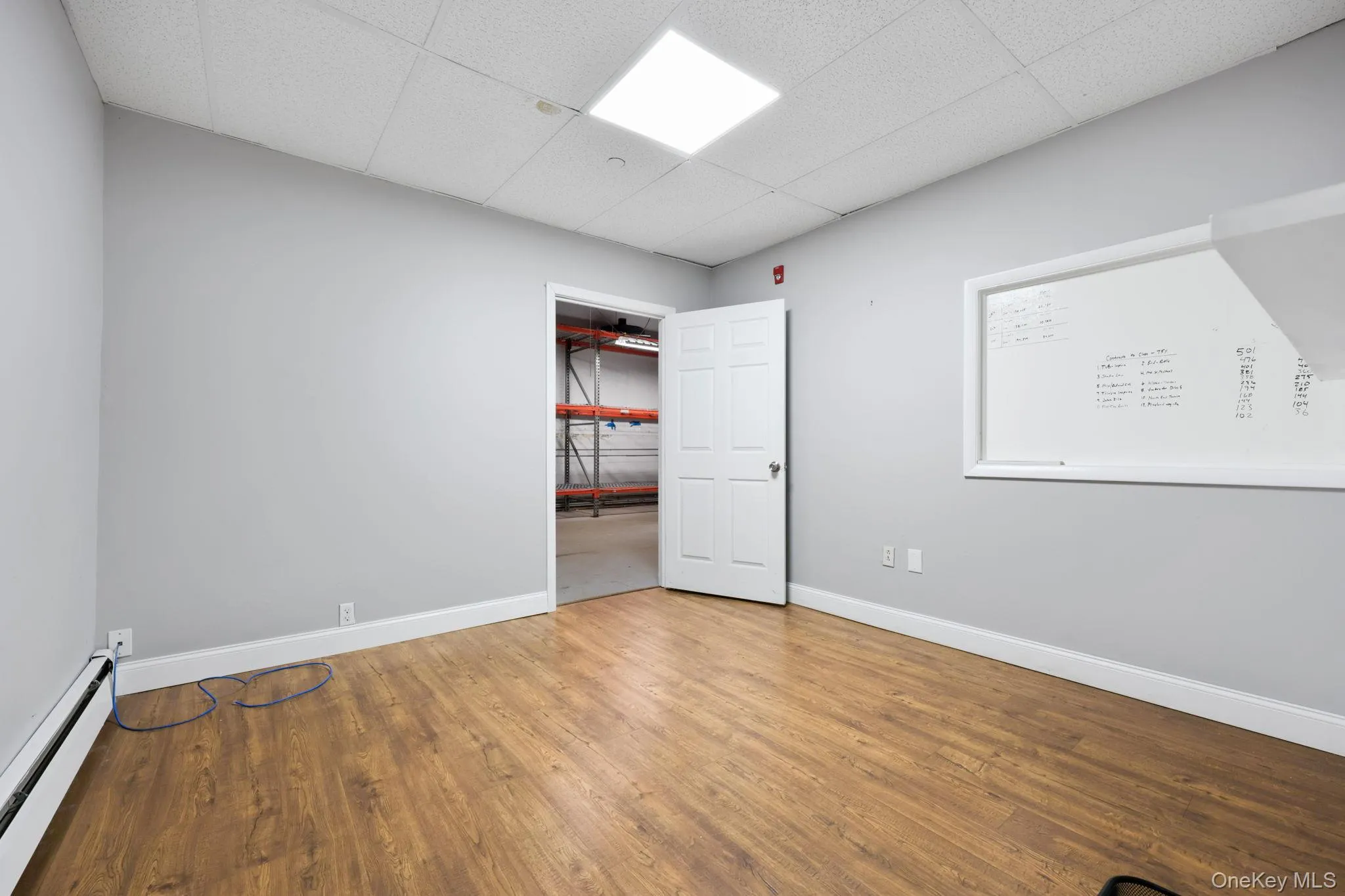 Unfurnished room with a baseboard radiator, a drop ceiling, and wood finished floors Unfurnished room with a baseboard radiator, a drop ceiling, and wood finished floors
