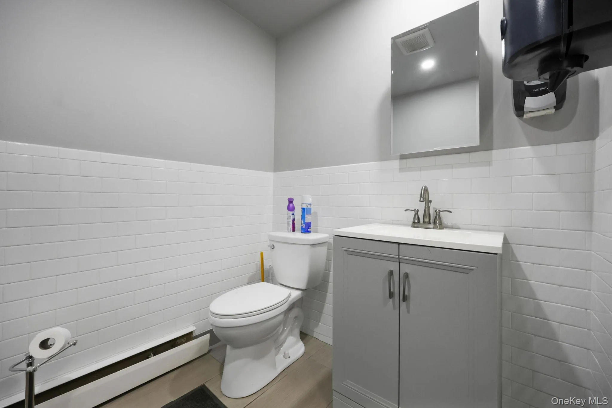 Bathroom featuring tile walls, wainscoting, vanity, and a baseboard heating unit Bathroom featuring tile walls, wainscoting, vanity, and a baseboard heating unit