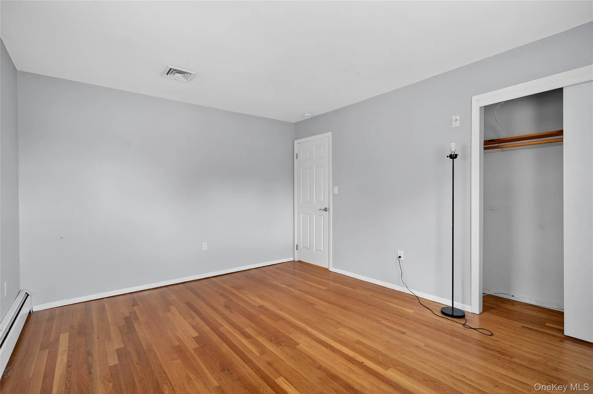 Unfurnished bedroom featuring a baseboard radiator, light wood-style floors, and a closet Unfurnished bedroom featuring a baseboard radiator, light wood-style floors, and a closet