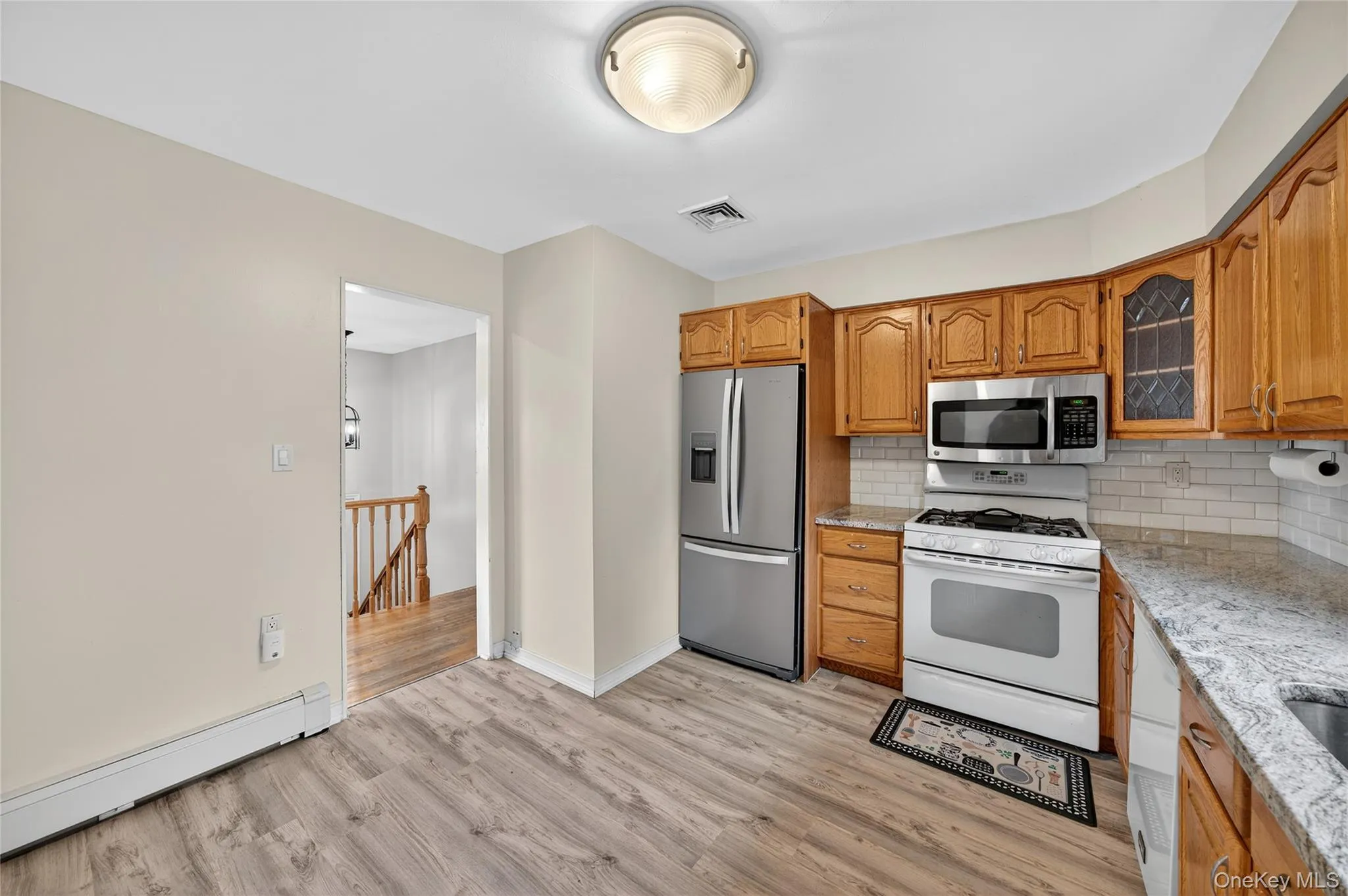Kitchen featuring appliances with stainless steel finishes, a baseboard heating unit, backsplash, brown cabinetry, and light wood-style floors Kitchen featuring appliances with stainless steel finishes, a baseboard heating unit, backsplash, brown cabinetry, and light wood-style floors