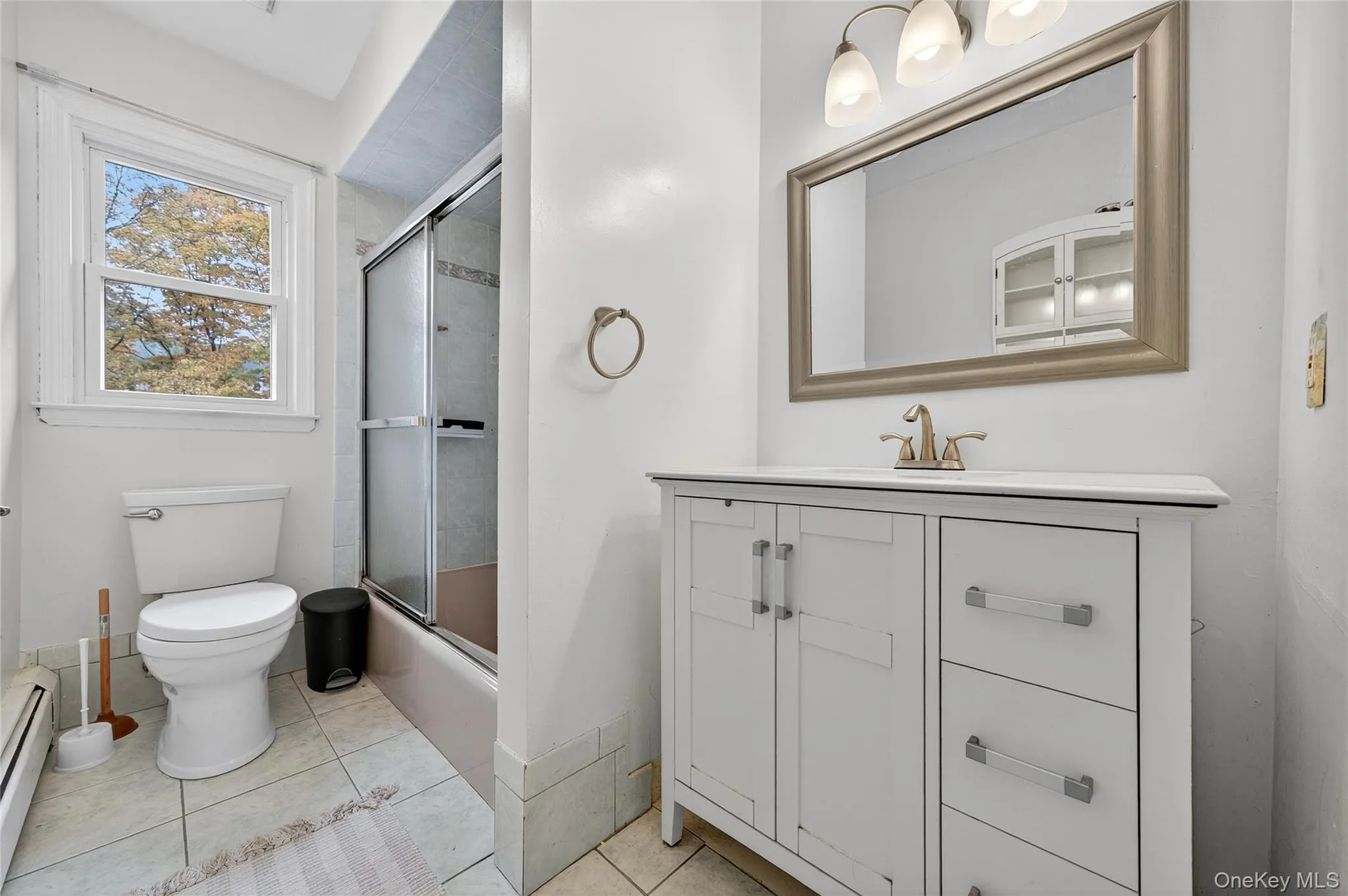 Bathroom with vanity, a baseboard heating unit, shower / bath combination with glass door, and light tile patterned flooring Bathroom with vanity, a baseboard heating unit, shower / bath combination with glass door, and light tile patterned flooring