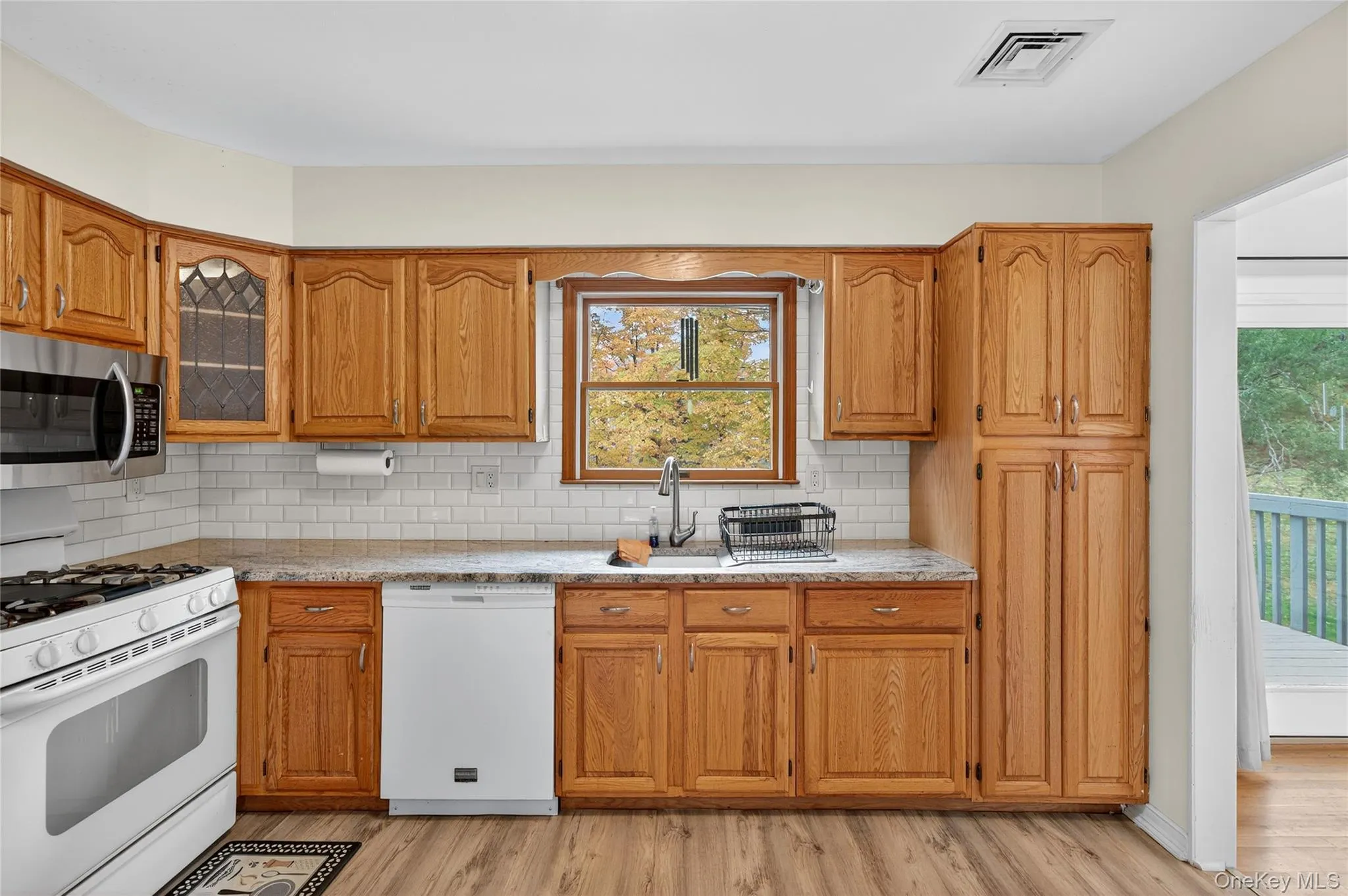 Kitchen featuring white appliances, backsplash, brown cabinetry, light wood-style flooring, and glass insert cabinets Kitchen featuring white appliances, backsplash, brown cabinetry, light wood-style flooring, and glass insert cabinets