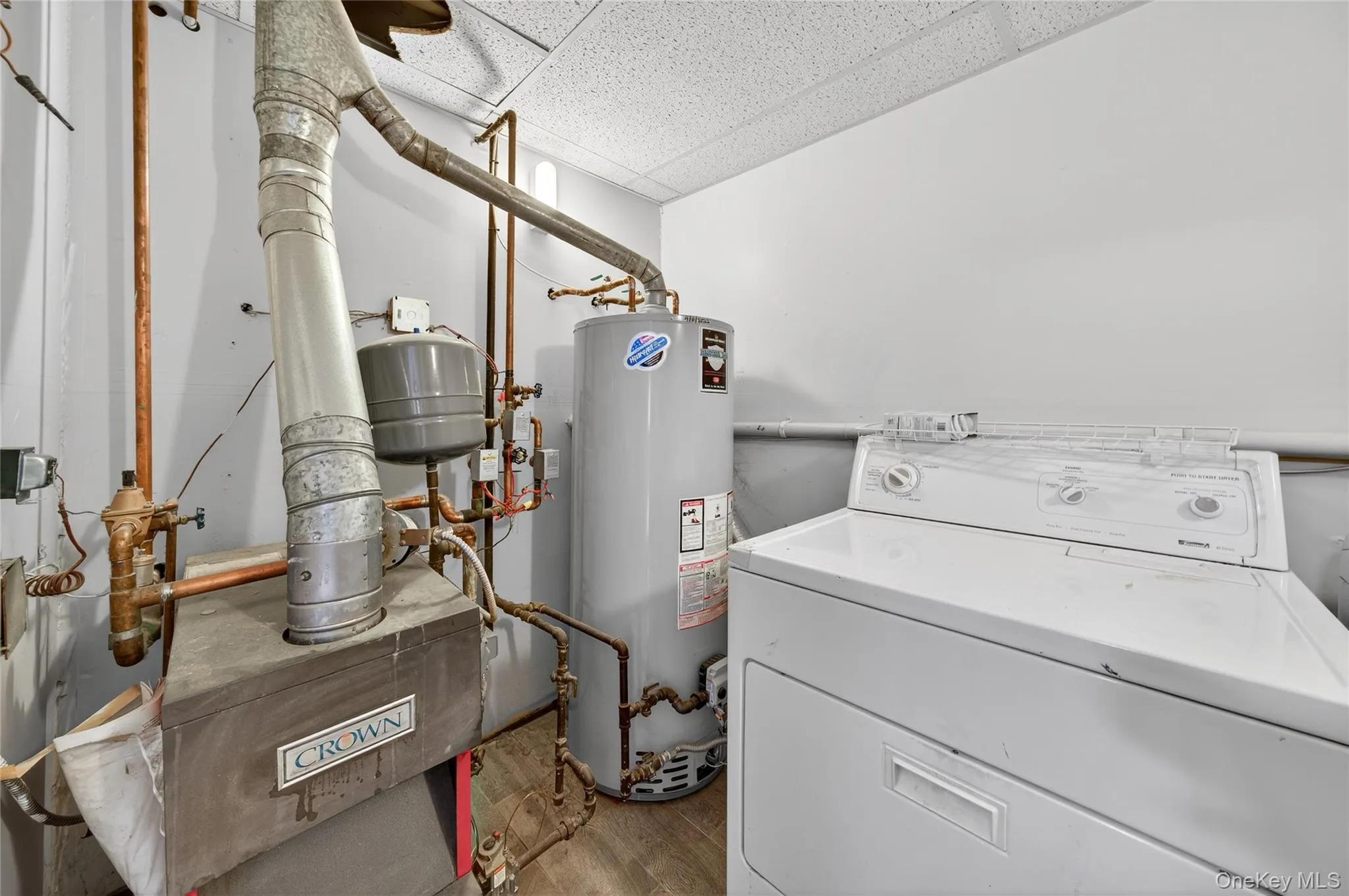 Laundry area featuring washer / dryer, light wood-type flooring, water heater, and a drop ceiling Laundry area featuring washer / dryer, light wood-type flooring, water heater, and a drop ceiling