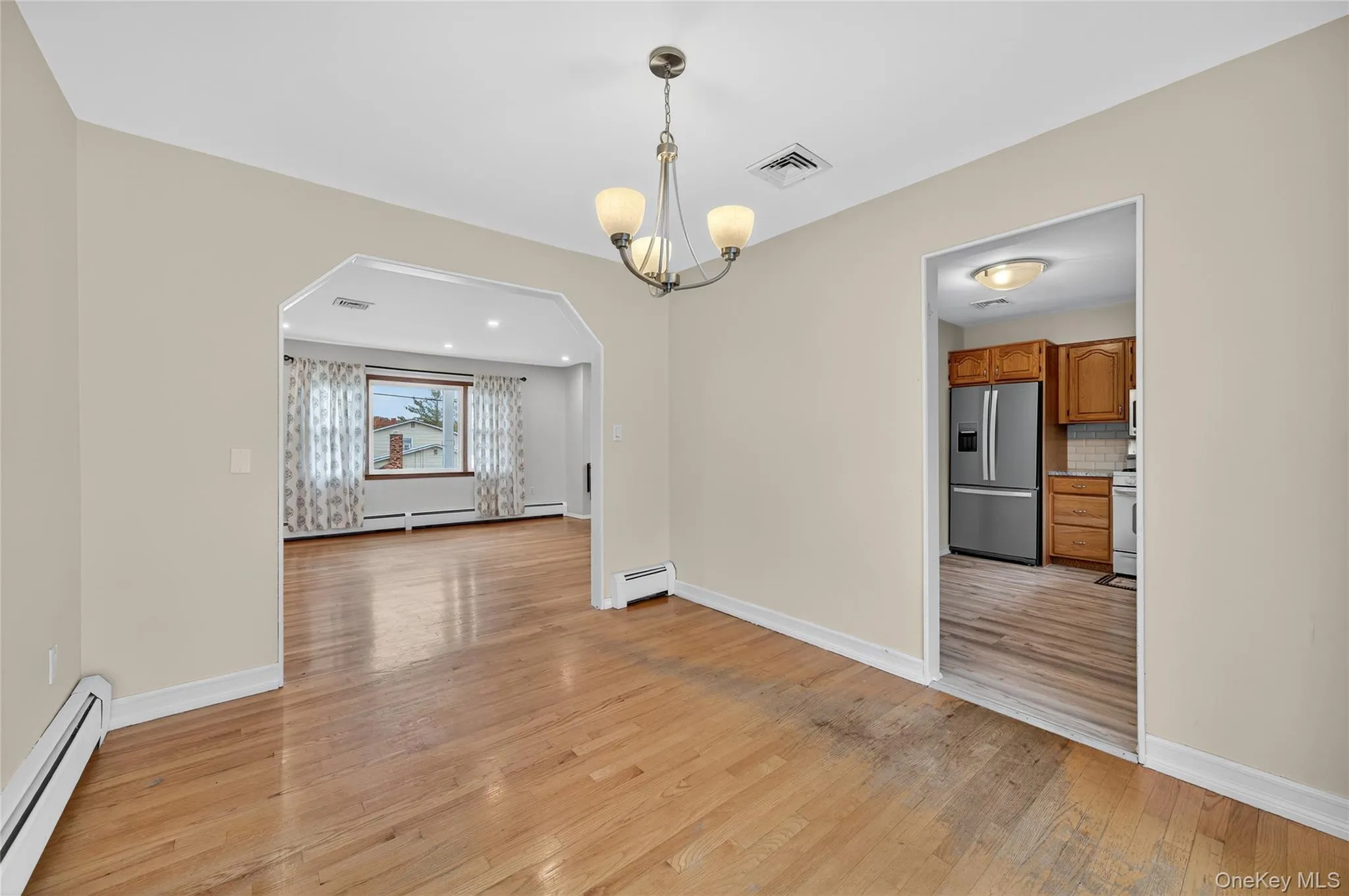 Unfurnished dining area with arched walkways, a baseboard radiator, light wood-style floors, and a chandelier Unfurnished dining area with arched walkways, a baseboard radiator, light wood-style floors, and a chandelier