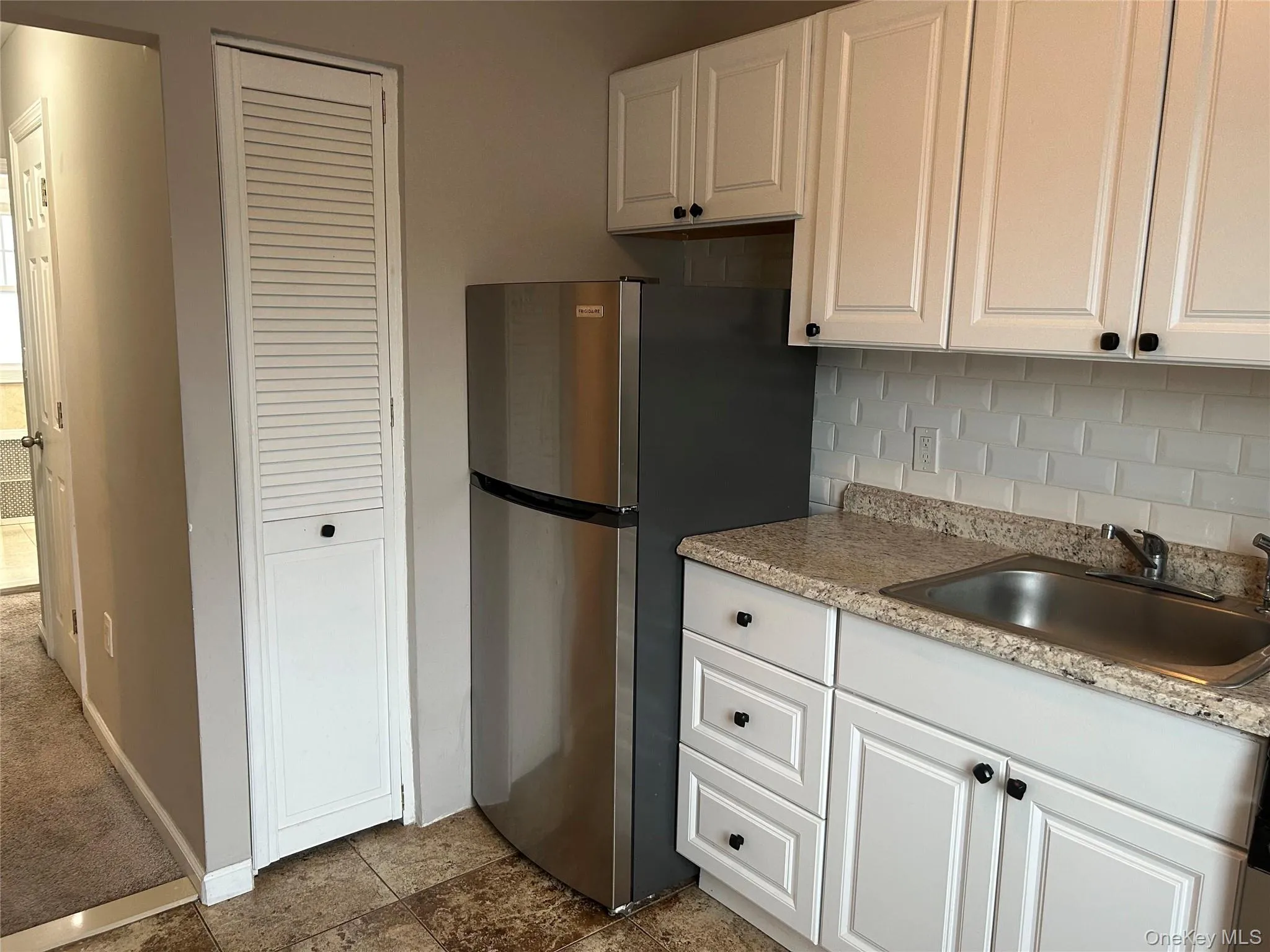 Kitchen featuring white cabinets, tasteful backsplash, freestanding refrigerator and a pantry closet Kitchen featuring white cabinets, tasteful backsplash, freestanding refrigerator and a pantry closet