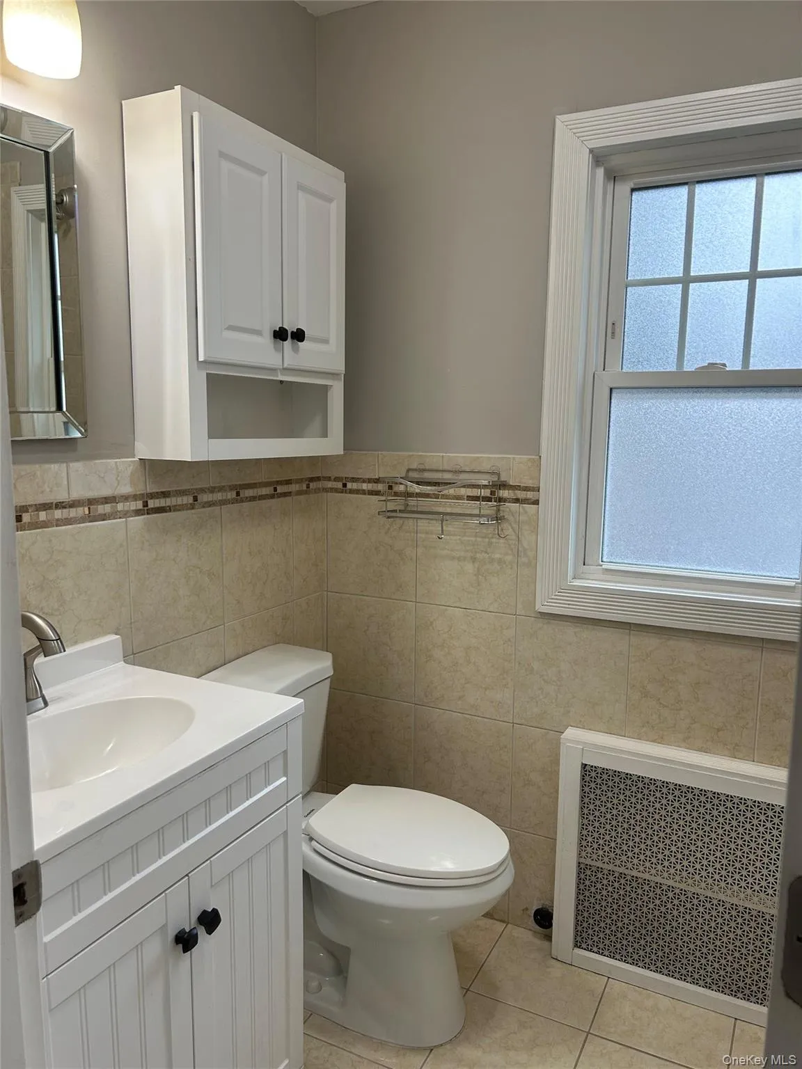 Full bathroom featuring vanity, white tub, light tile patterned floors, radiator and tile walls Full bathroom featuring vanity, white tub, light tile patterned floors, radiator and tile walls