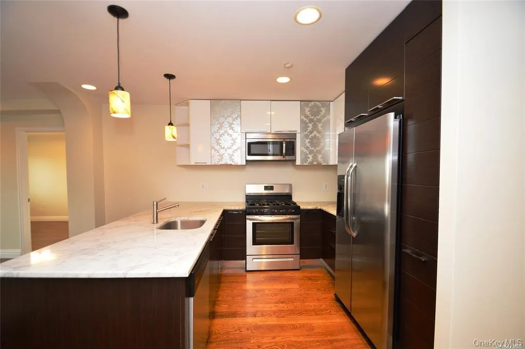 Kitchen featuring open shelves, appliances with stainless steel finishes, light wood-style floors, a peninsula, and hanging light fixtures Kitchen featuring open shelves, appliances with stainless steel finishes, light wood-style floors, a peninsula, and hanging light fixtures