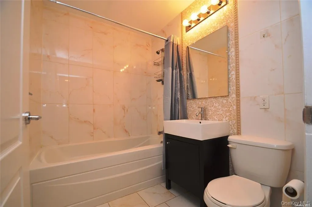 Full bathroom with vanity, shower / bath combo, and tile walls Full bathroom with vanity, shower / bath combo, and tile walls