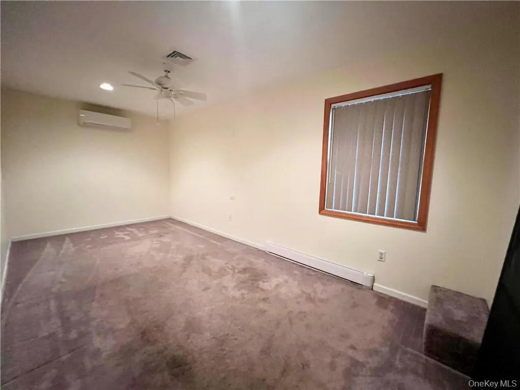 Carpeted empty room featuring a baseboard heating unit, ceiling fan, recessed lighting, and a wall mounted air conditioner Carpeted empty room featuring a baseboard heating unit, ceiling fan, recessed lighting, and a wall mounted air conditioner
