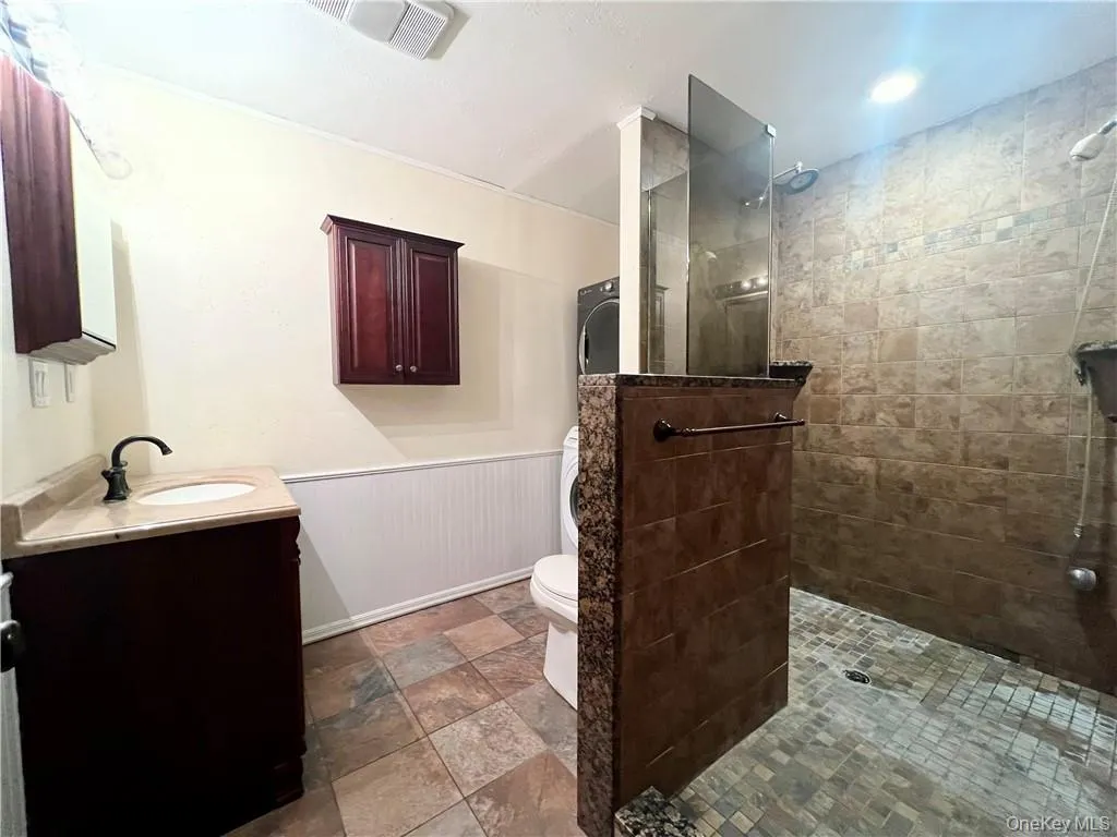 Bathroom with wainscoting, vanity, a walk in shower, and stone finish floors Bathroom with wainscoting, vanity, a walk in shower, and stone finish floors