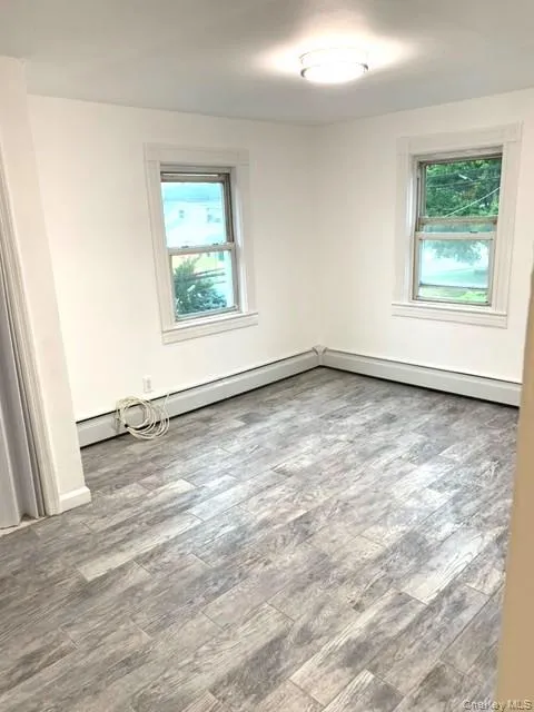 Spare room with wood finished floors, plenty of natural light, and a baseboard heating unit Spare room with wood finished floors, plenty of natural light, and a baseboard heating unit