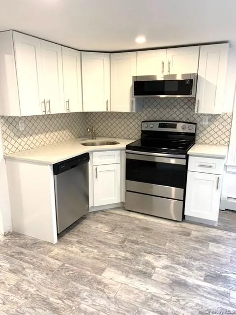 Kitchen with appliances with stainless steel finishes, white cabinetry, backsplash, light wood finished floors, and a baseboard radiator Kitchen with appliances with stainless steel finishes, white cabinetry, backsplash, light wood finished floors, and a baseboard radiator