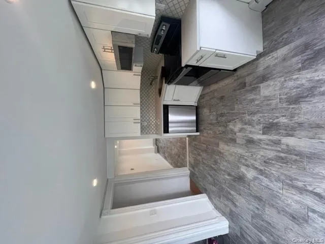 Kitchen with white cabinets, range, dark wood-style flooring, stainless steel dishwasher, and light stone countertops Kitchen with white cabinets, range, dark wood-style flooring, stainless steel dishwasher, and light stone countertops