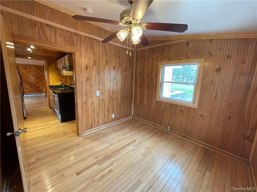 Unfurnished room with wooden walls, ornamental molding, and light wood-style flooring Unfurnished room with wooden walls, ornamental molding, and light wood-style flooring