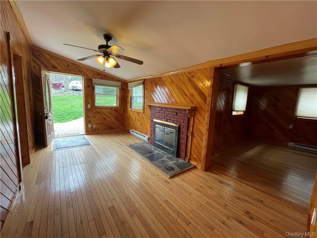 Unfurnished living room featuring wooden walls, a fireplace, hardwood / wood-style floors, lofted ceiling, and a baseboard radiator Unfurnished living room featuring wooden walls, a fireplace, hardwood / wood-style floors, lofted ceiling, and a baseboard radiator