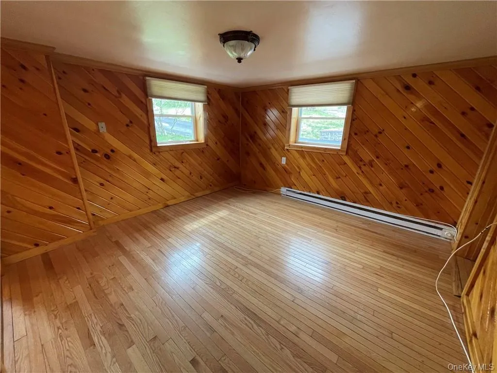 Spare room with wooden walls, a baseboard heating unit, and hardwood / wood-style flooring Spare room with wooden walls, a baseboard heating unit, and hardwood / wood-style flooring