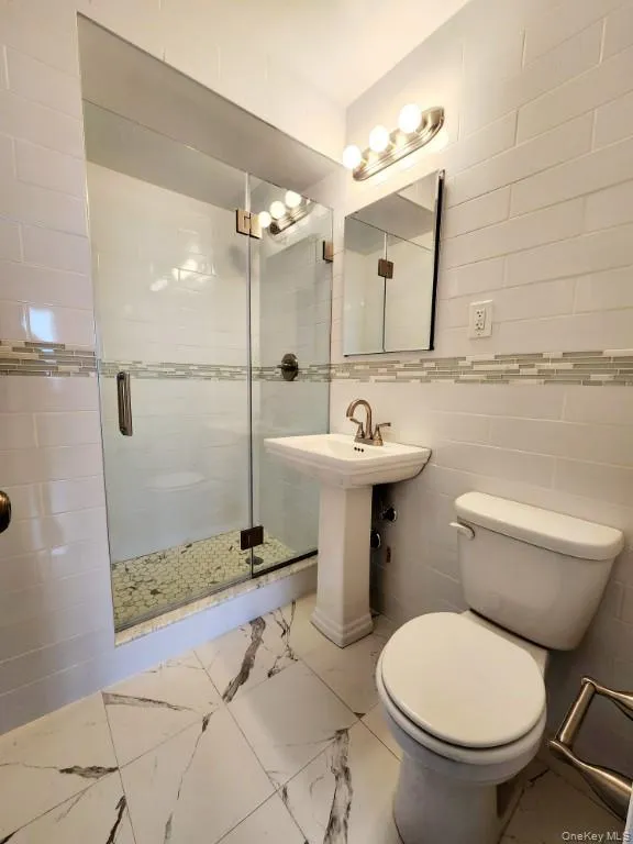 Bathroom featuring tile walls, a stall shower, and marble look tile flooring Bathroom featuring tile walls, a stall shower, and marble look tile flooring