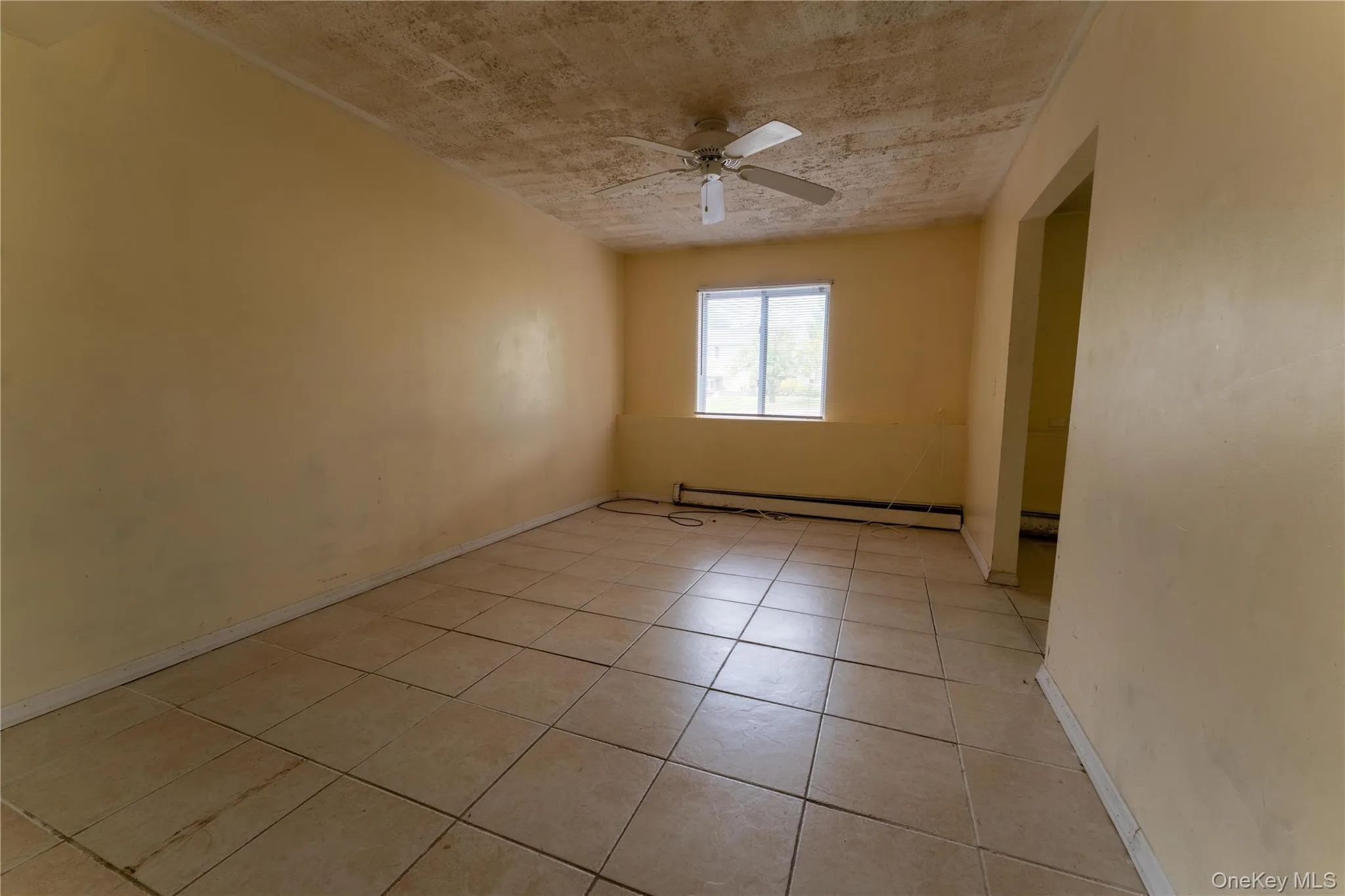 Empty room featuring light tile patterned floors, a baseboard heating unit, and ceiling fan Empty room featuring light tile patterned floors, a baseboard heating unit, and ceiling fan