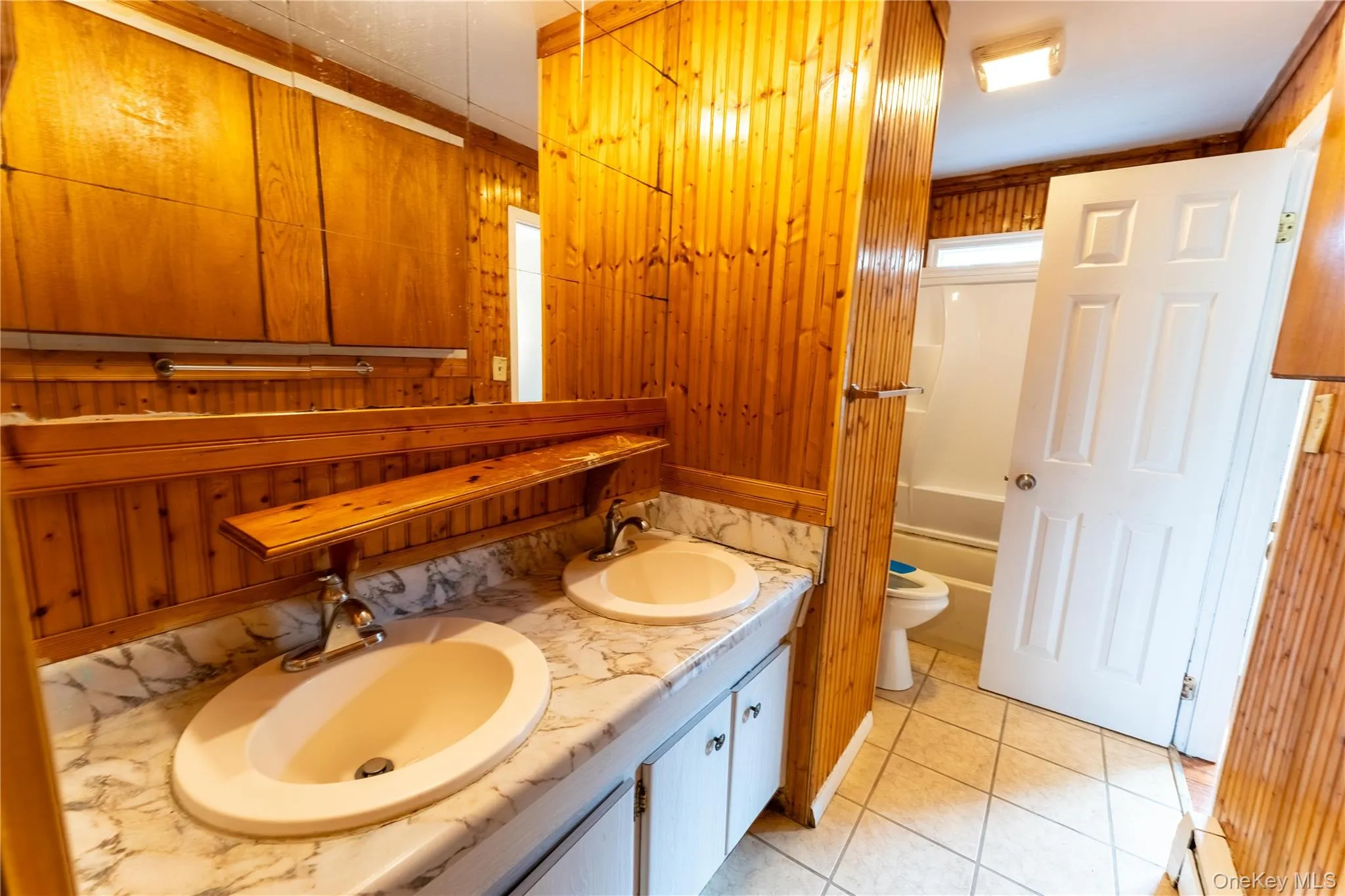 Full bathroom featuring wooden walls, double vanity, light tile patterned floors, and bathing tub / shower combination Full bathroom featuring wooden walls, double vanity, light tile patterned floors, and bathing tub / shower combination