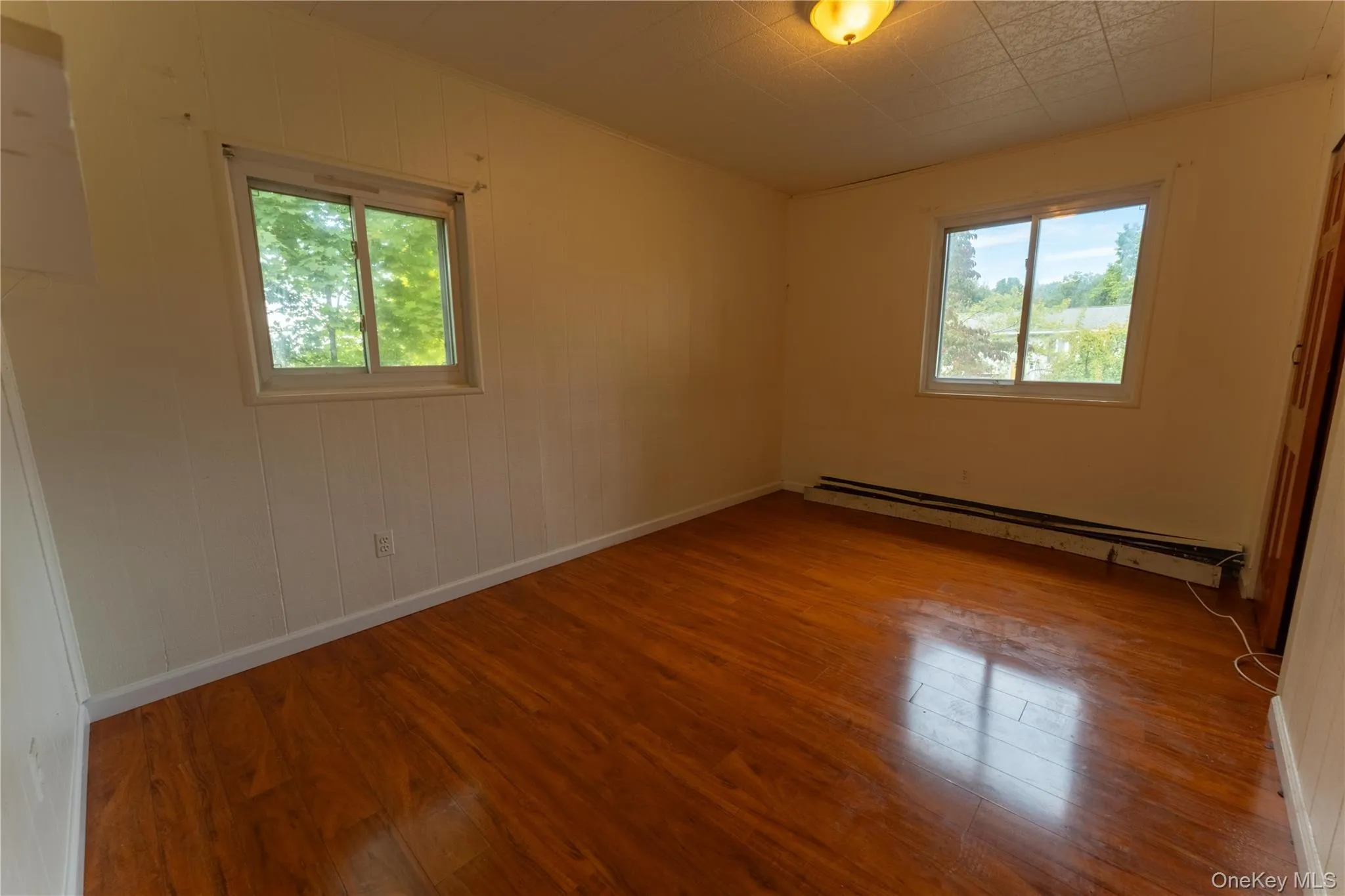 Unfurnished room with wood finished floors, a baseboard heating unit, plenty of natural light, crown molding, and wooden walls Unfurnished room with wood finished floors, a baseboard heating unit, plenty of natural light, crown molding, and wooden walls