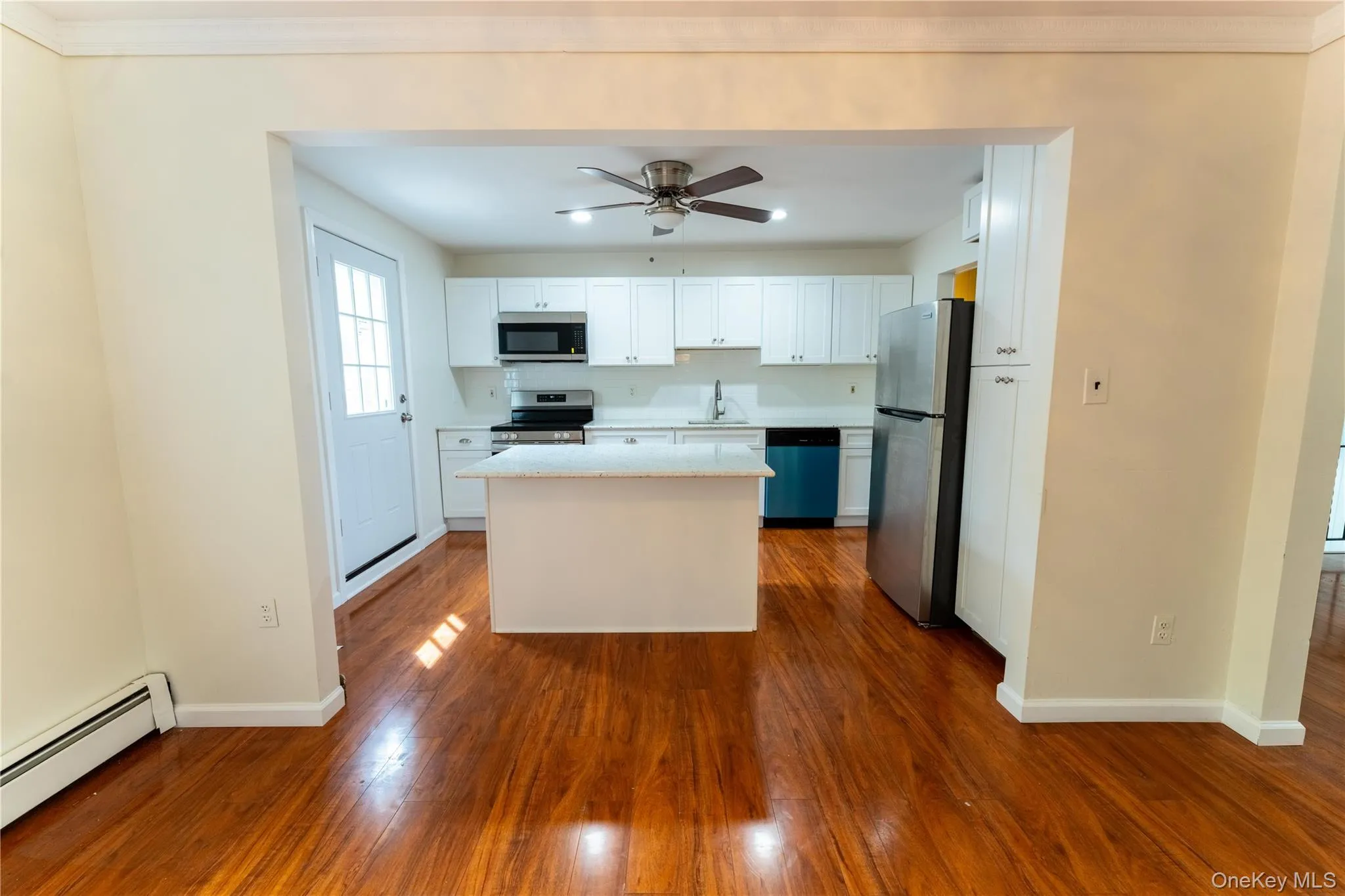 Kitchen featuring white cabinets, appliances with stainless steel finishes, a center island, dark wood-style flooring, and light stone counters Kitchen featuring white cabinets, appliances with stainless steel finishes, a center island, dark wood-style flooring, and light stone counters