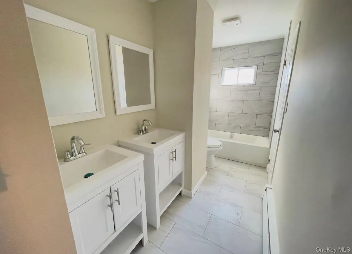 Full bathroom with two vanities, baseboard heating, light marble finish floors, and shower / bathtub combination Full bathroom with two vanities, baseboard heating, light marble finish floors, and shower / bathtub combination