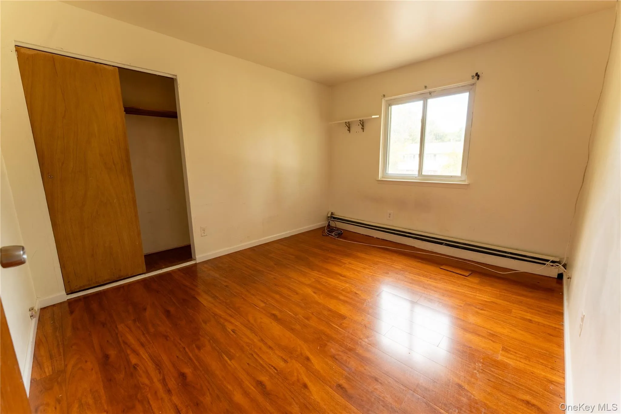 Unfurnished bedroom featuring baseboard heating, light wood-type flooring, and a closet Unfurnished bedroom featuring baseboard heating, light wood-type flooring, and a closet