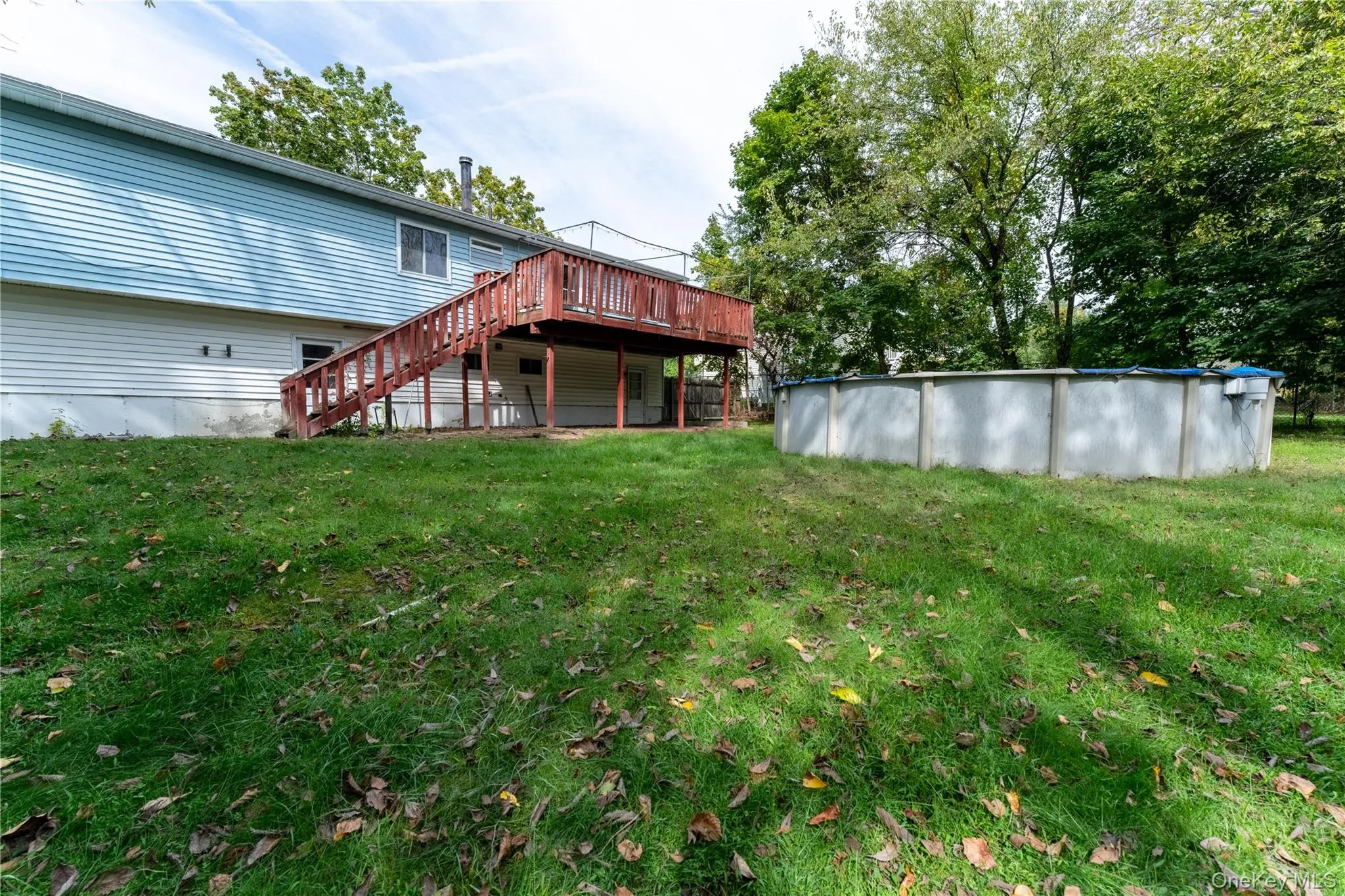 Rear view of property featuring stairs, a wooden deck, a lawn, and a covered pool Rear view of property featuring stairs, a wooden deck, a lawn, and a covered pool