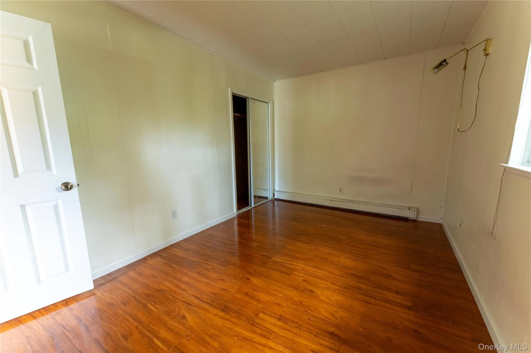 Unfurnished room with dark wood-style flooring and a baseboard heating unit Unfurnished room with dark wood-style flooring and a baseboard heating unit
