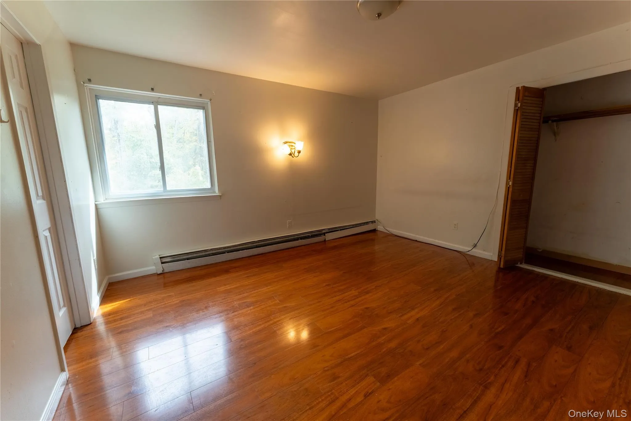 Unfurnished bedroom with wood finished floors, a baseboard heating unit, and a closet Unfurnished bedroom with wood finished floors, a baseboard heating unit, and a closet