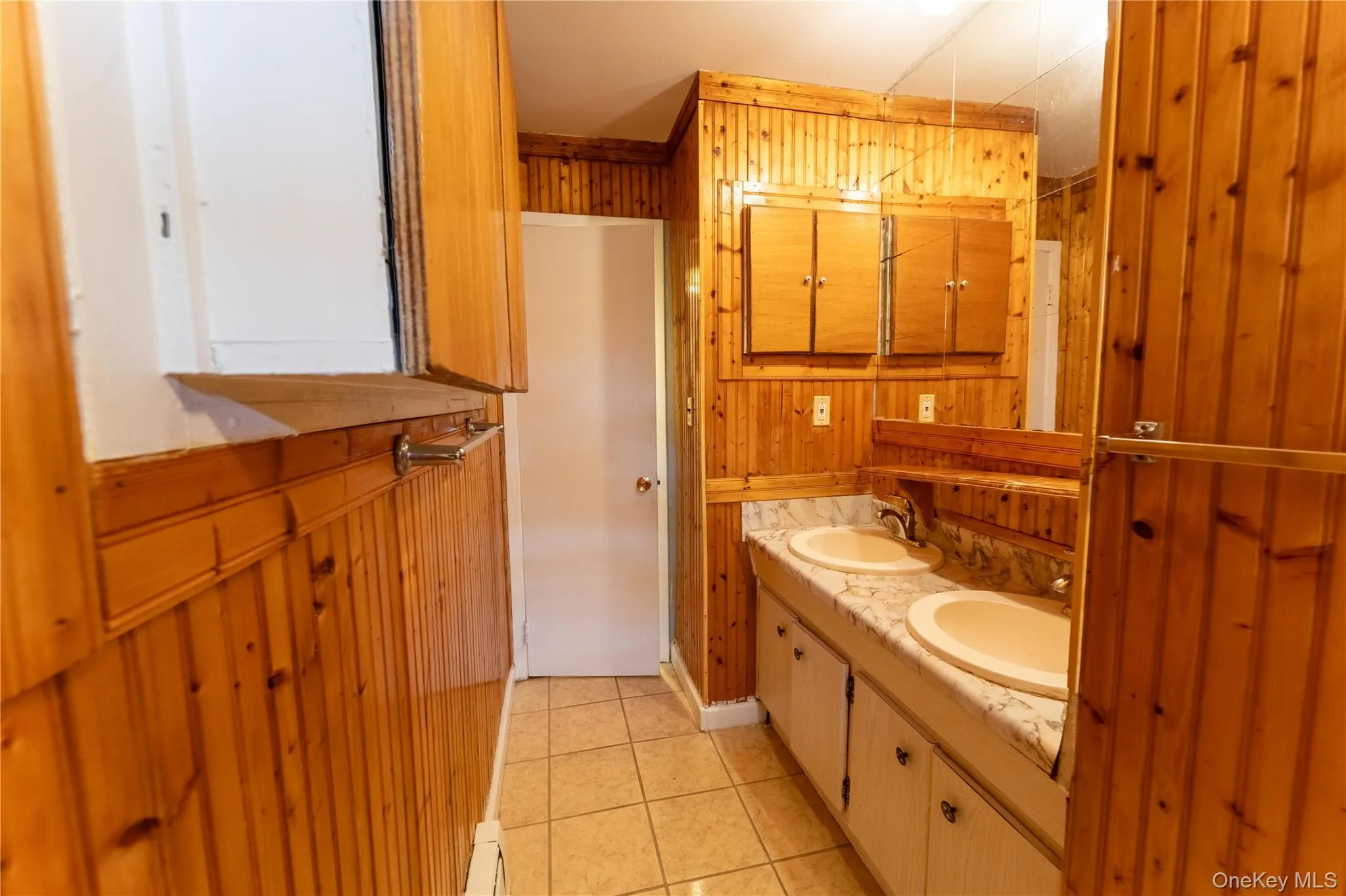 Bathroom featuring wooden walls, light tile patterned floors, double vanity, and a baseboard heating unit Bathroom featuring wooden walls, light tile patterned floors, double vanity, and a baseboard heating unit