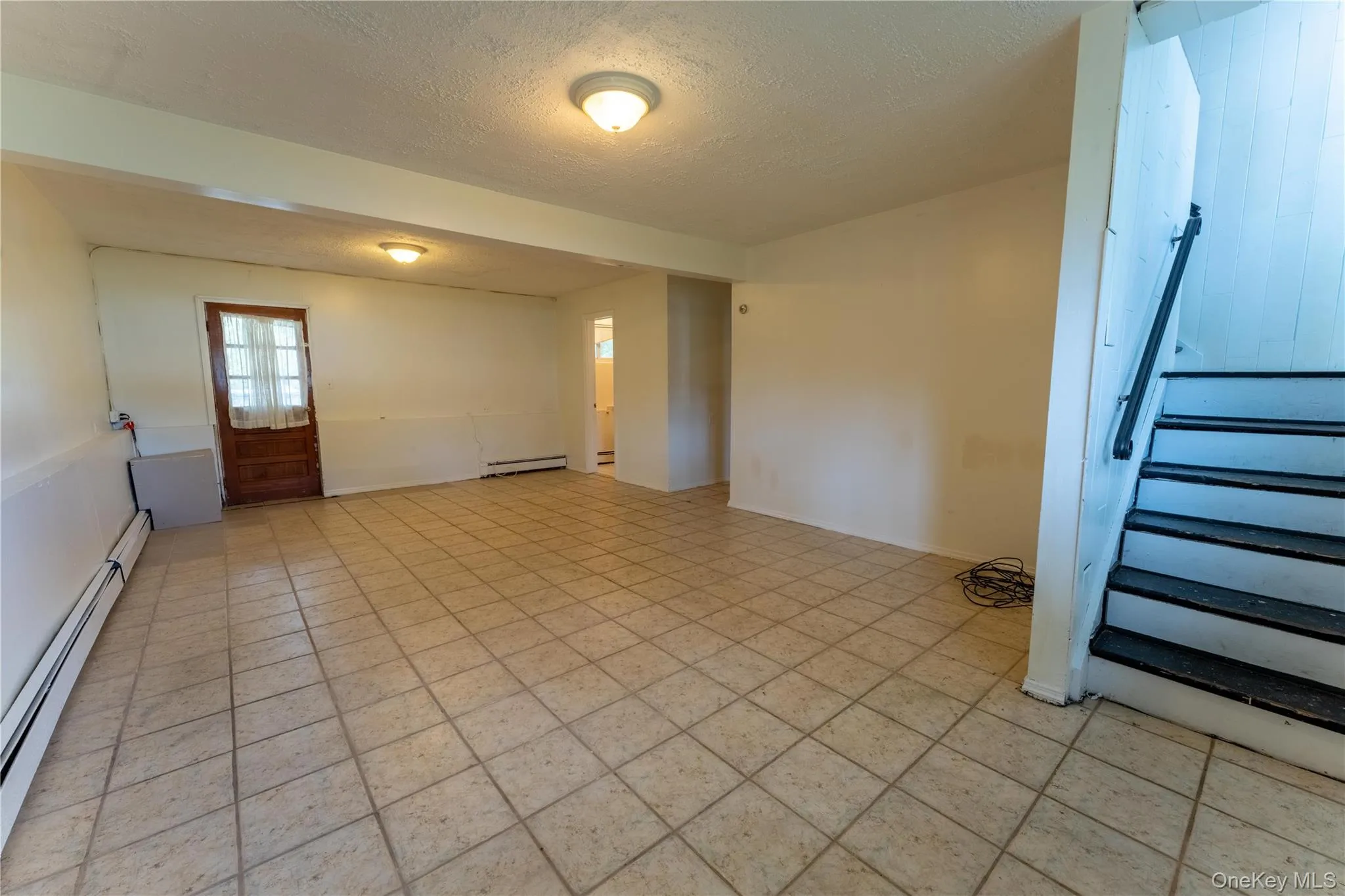 Unfurnished room with baseboard heating, a textured ceiling, stairway, and light tile patterned floors Unfurnished room with baseboard heating, a textured ceiling, stairway, and light tile patterned floors