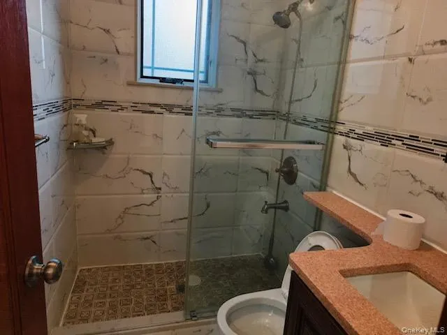 Bathroom featuring vanity, a marble finish shower, and tile walls Bathroom featuring vanity, a marble finish shower, and tile walls