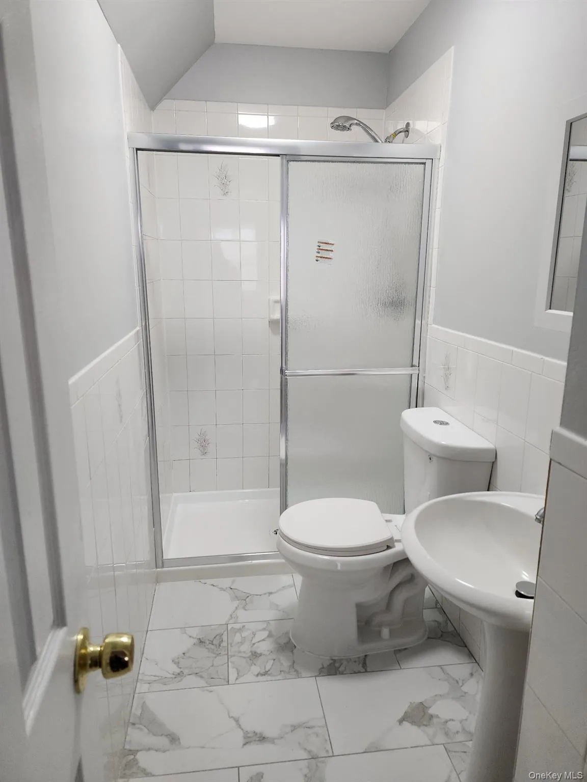 Bathroom with marble finish flooring, a stall shower, tile walls, and a wainscoted wall Bathroom with marble finish flooring, a stall shower, tile walls, and a wainscoted wall