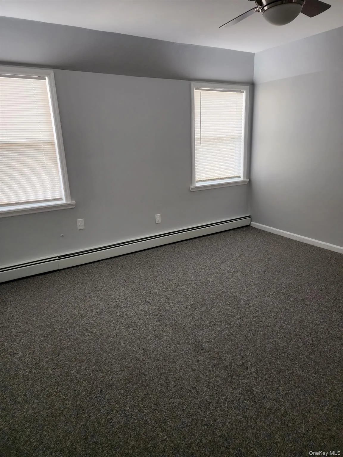Empty room with a baseboard heating unit, carpet floors, and ceiling fan Empty room with a baseboard heating unit, carpet floors, and ceiling fan