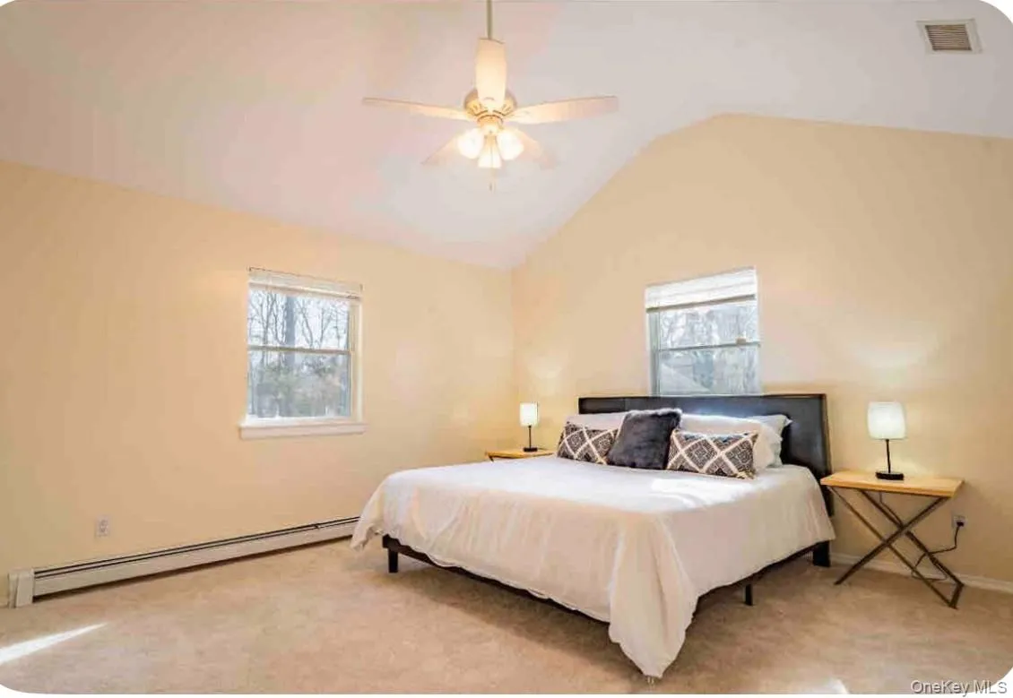 Carpeted bedroom featuring baseboard heating, vaulted ceiling, and ceiling fan Carpeted bedroom featuring baseboard heating, vaulted ceiling, and ceiling fan
