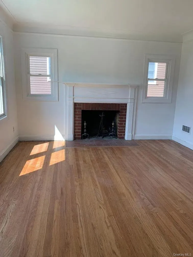 Unfurnished living room featuring wood finished floors, a brick fireplace, and baseboard heating Unfurnished living room featuring wood finished floors, a brick fireplace, and baseboard heating
